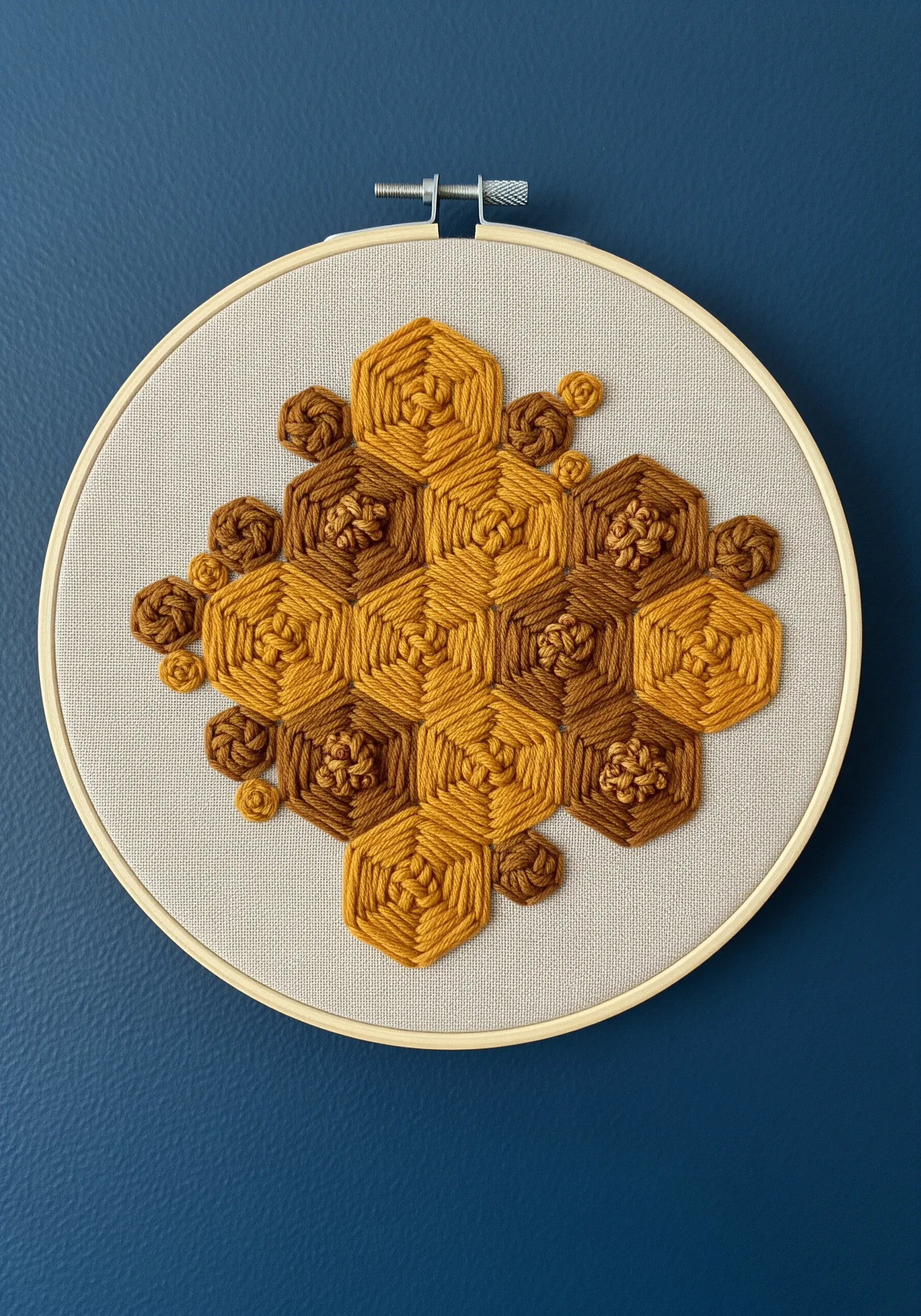 Geometric honeycomb pattern in shades of mustard and brown, using wrapped stitches and French knots.