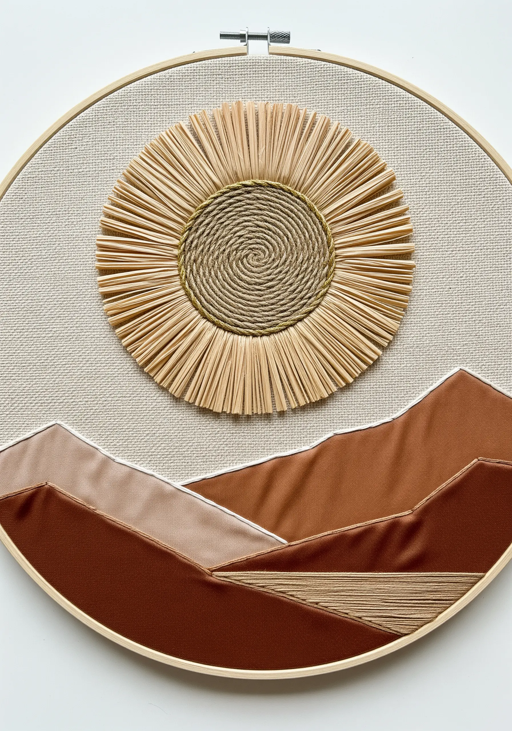 A landscape embroidery with a raffia sun and fabric appliqué mountains.
