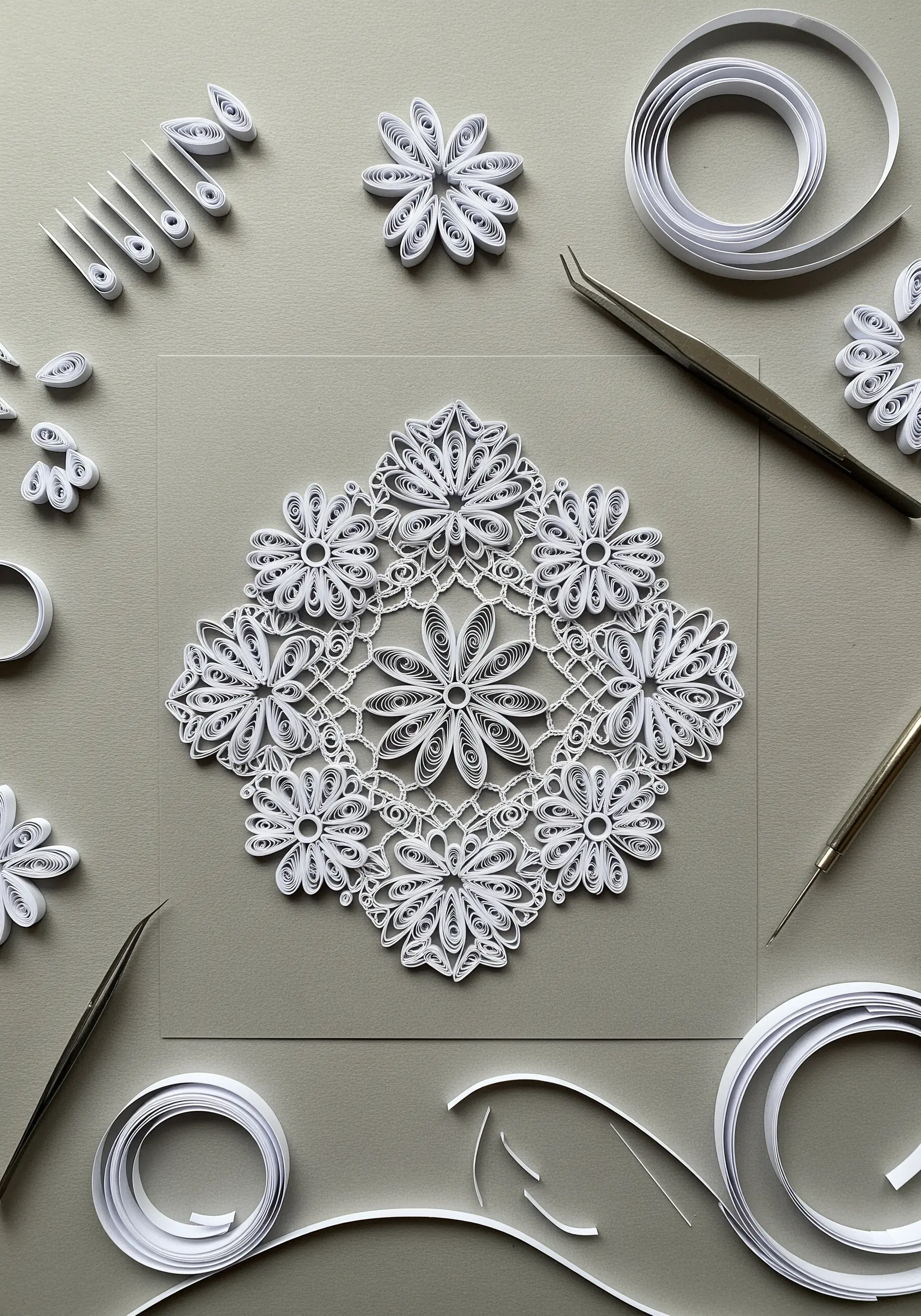 An intricate, lace-like mandala made from tightly coiled white paper strips on a gray background.
