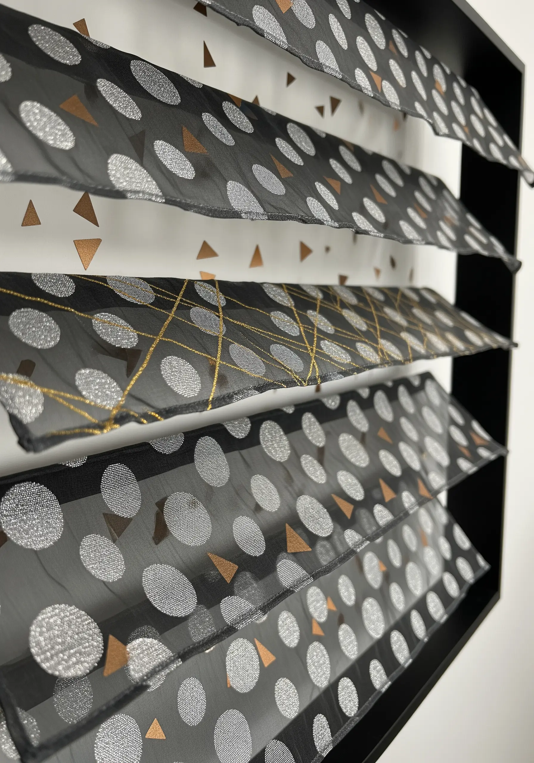 Gold metallic thread stitched in geometric patterns on sheer black fabric with silver polka dots.