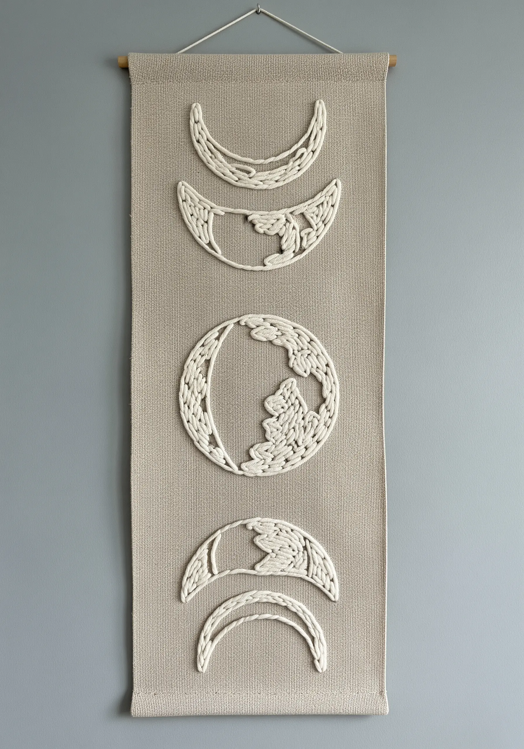 A wall hanging with moon phases created by couching thick white cord onto a neutral fabric.