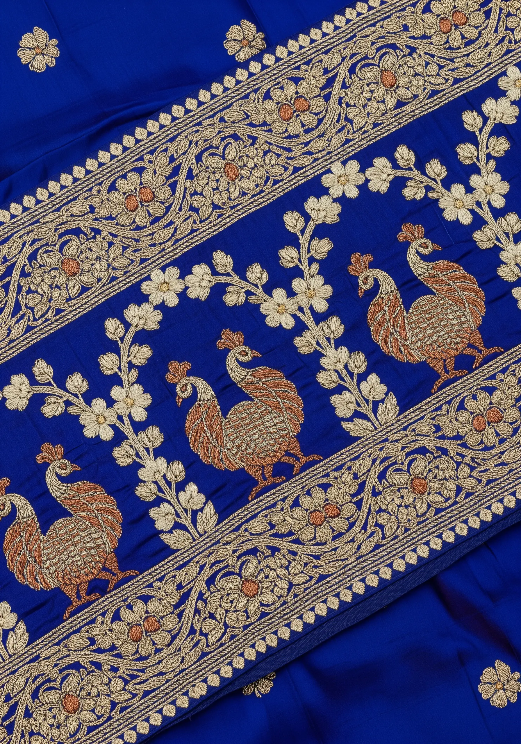 Traditional peacock border on a blue saree, filled with dense gold and copper stitches.