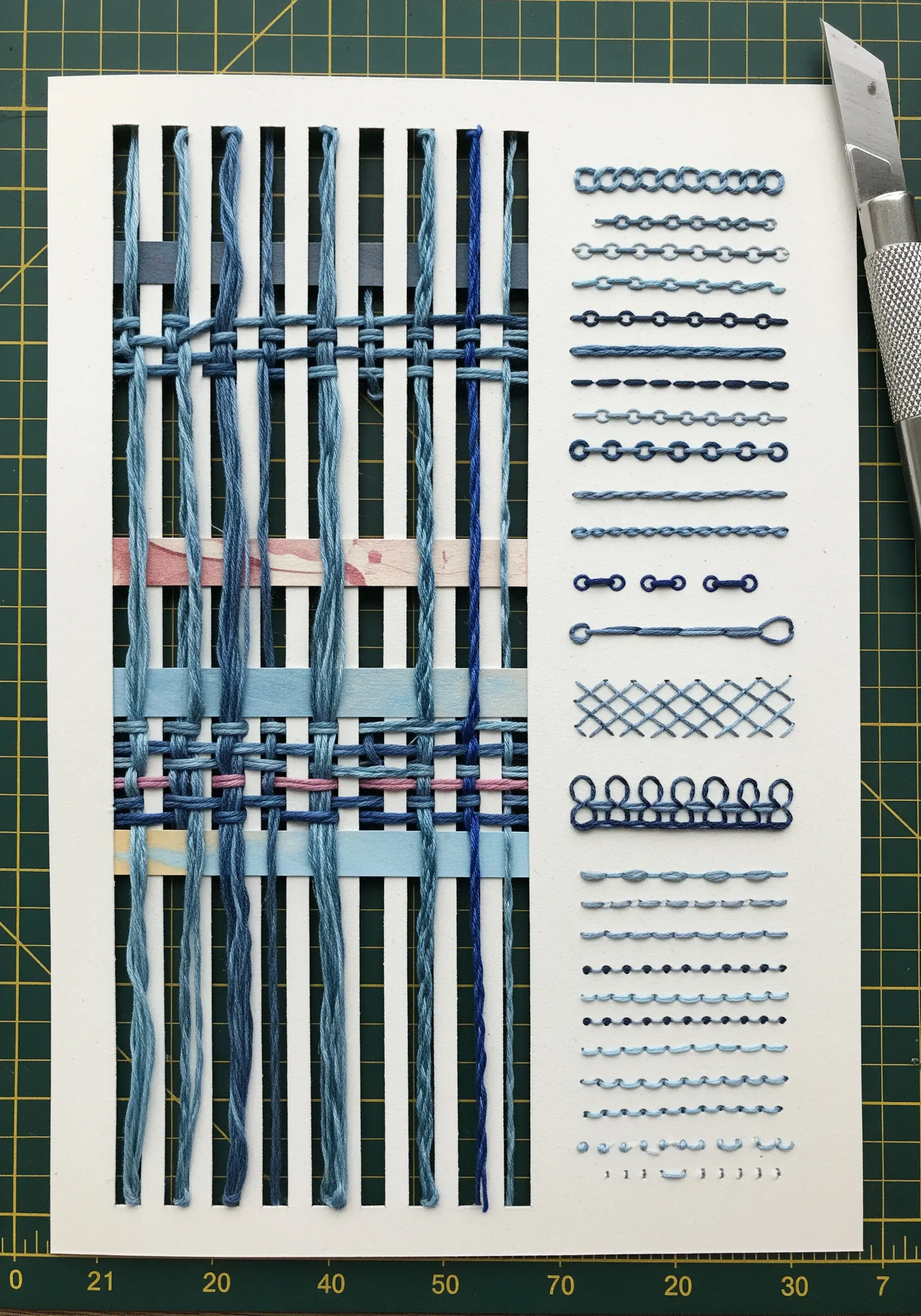 Threads and paper strips woven through a white card with vertical slits.