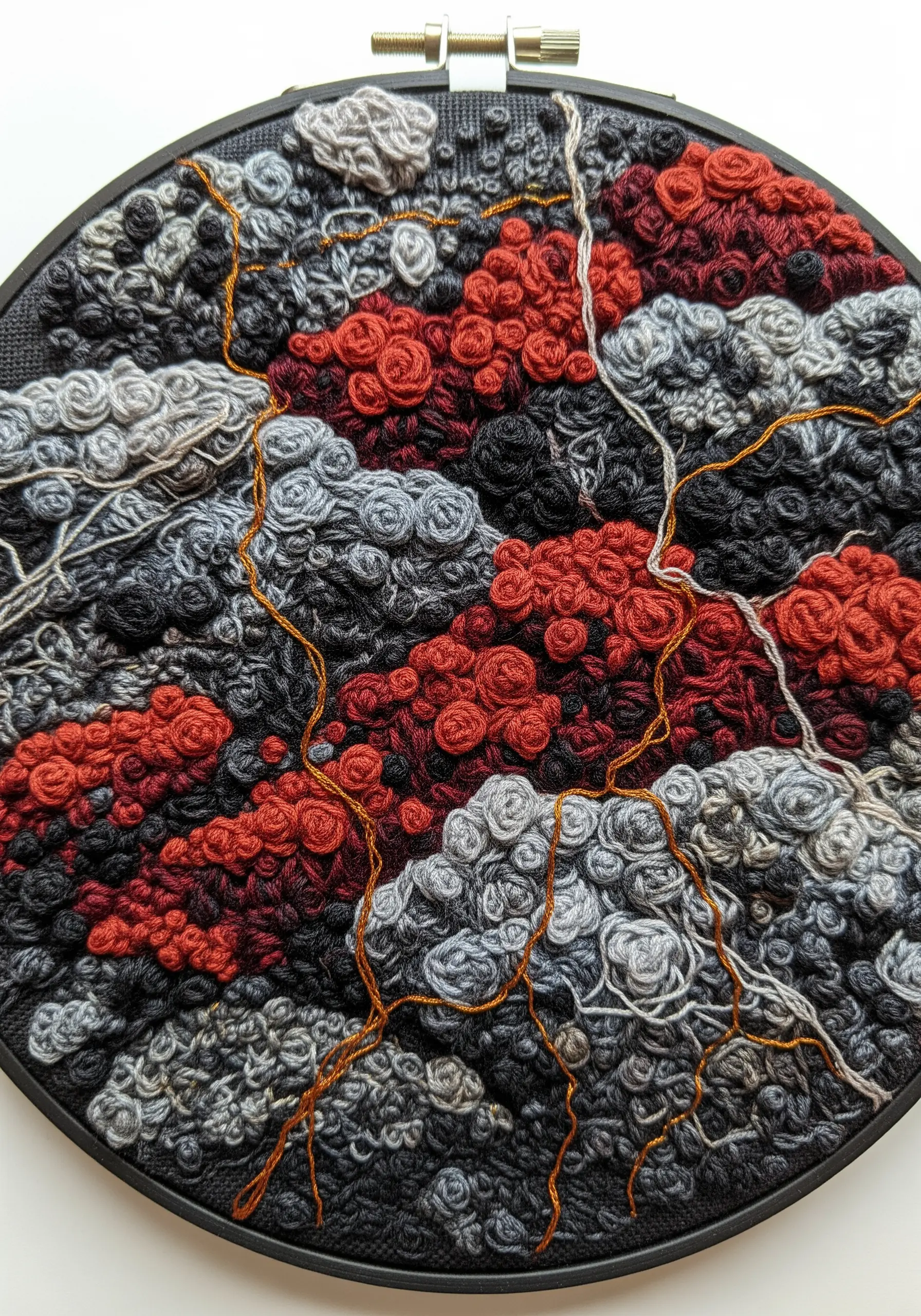 Abstract hoop art with dense, highly textured knots in red, gray, and black, resembling volcanic rock.