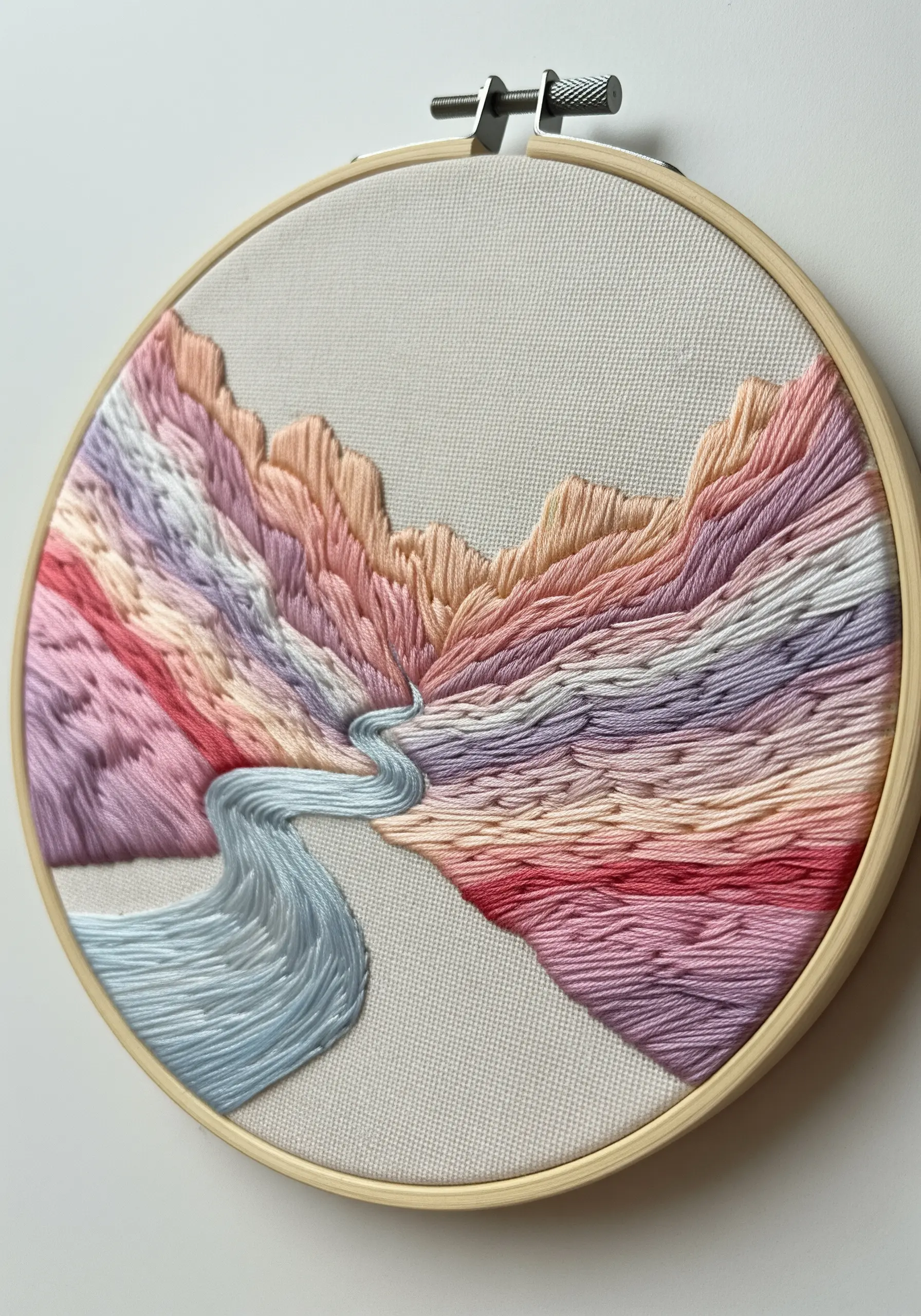 Abstract mountain landscape with a flowing river stitched in soft, blended pastel colors.