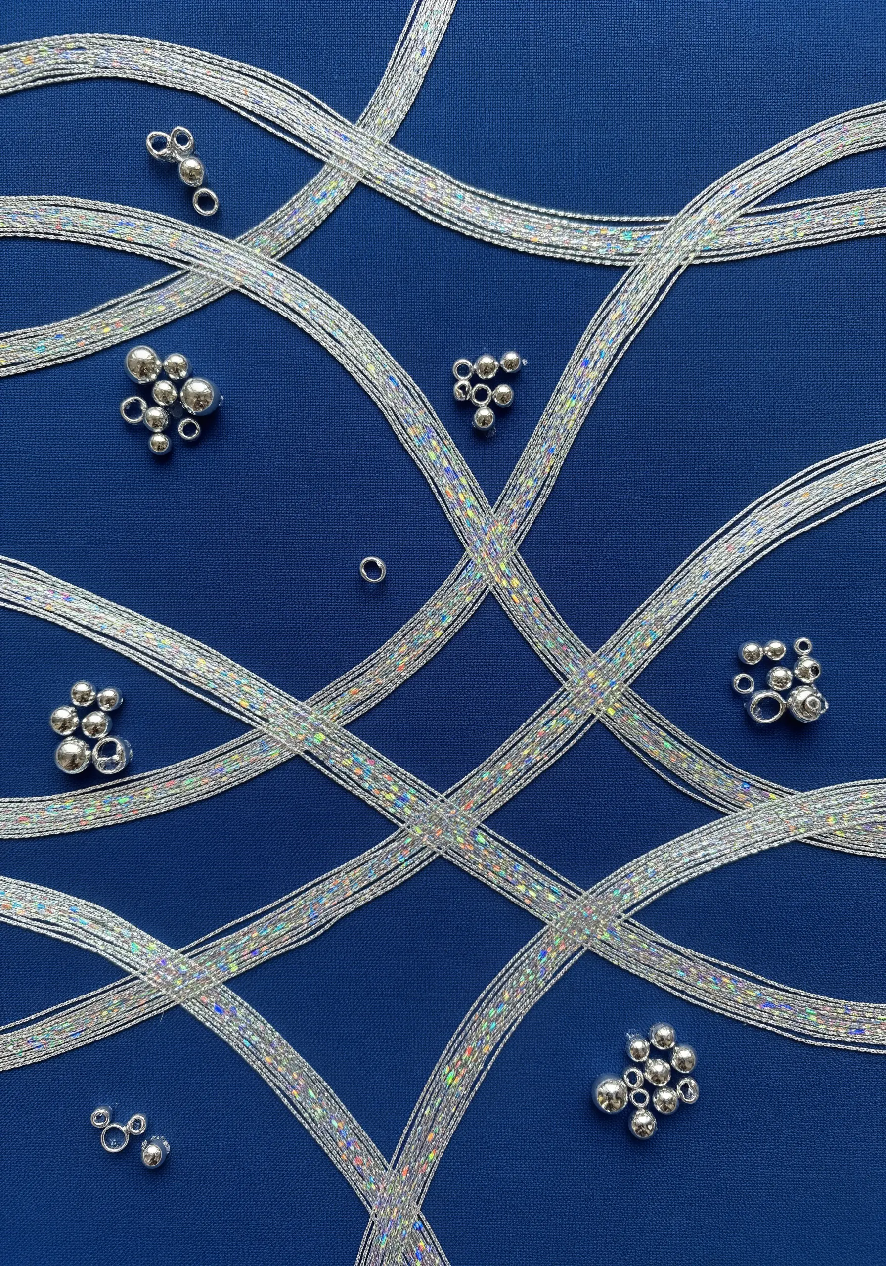 Woven holographic thread ribbons with silver bead clusters on a blue background.