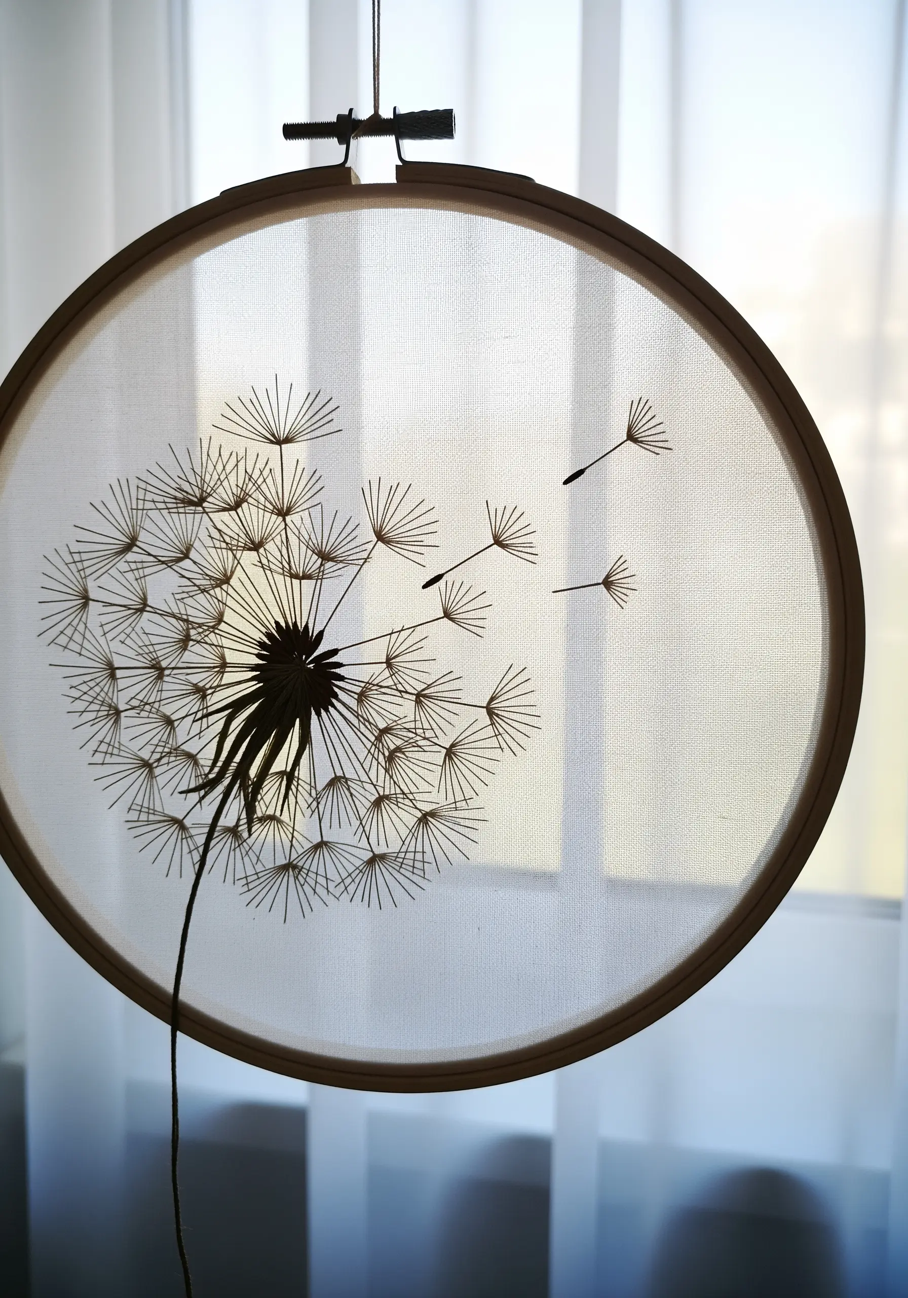 A dandelion stitched on sheer fabric in a hoop, creating a transparent, airy effect.