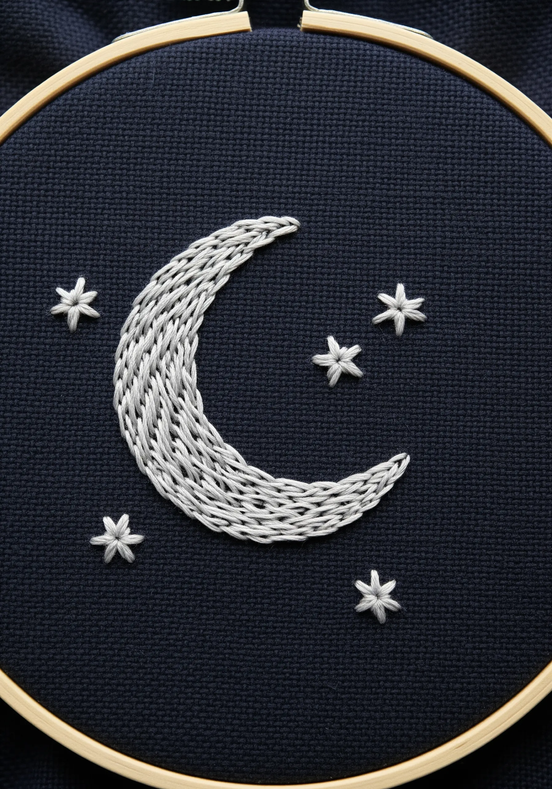 A crescent moon filled with textured, interlocking chain stitches on dark fabric.