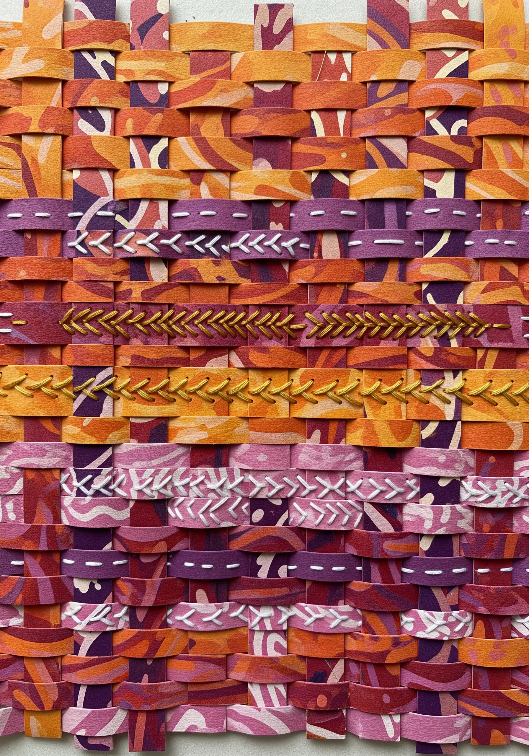 Woven paper strips in orange and purple, embellished with rows of decorative embroidery stitches.