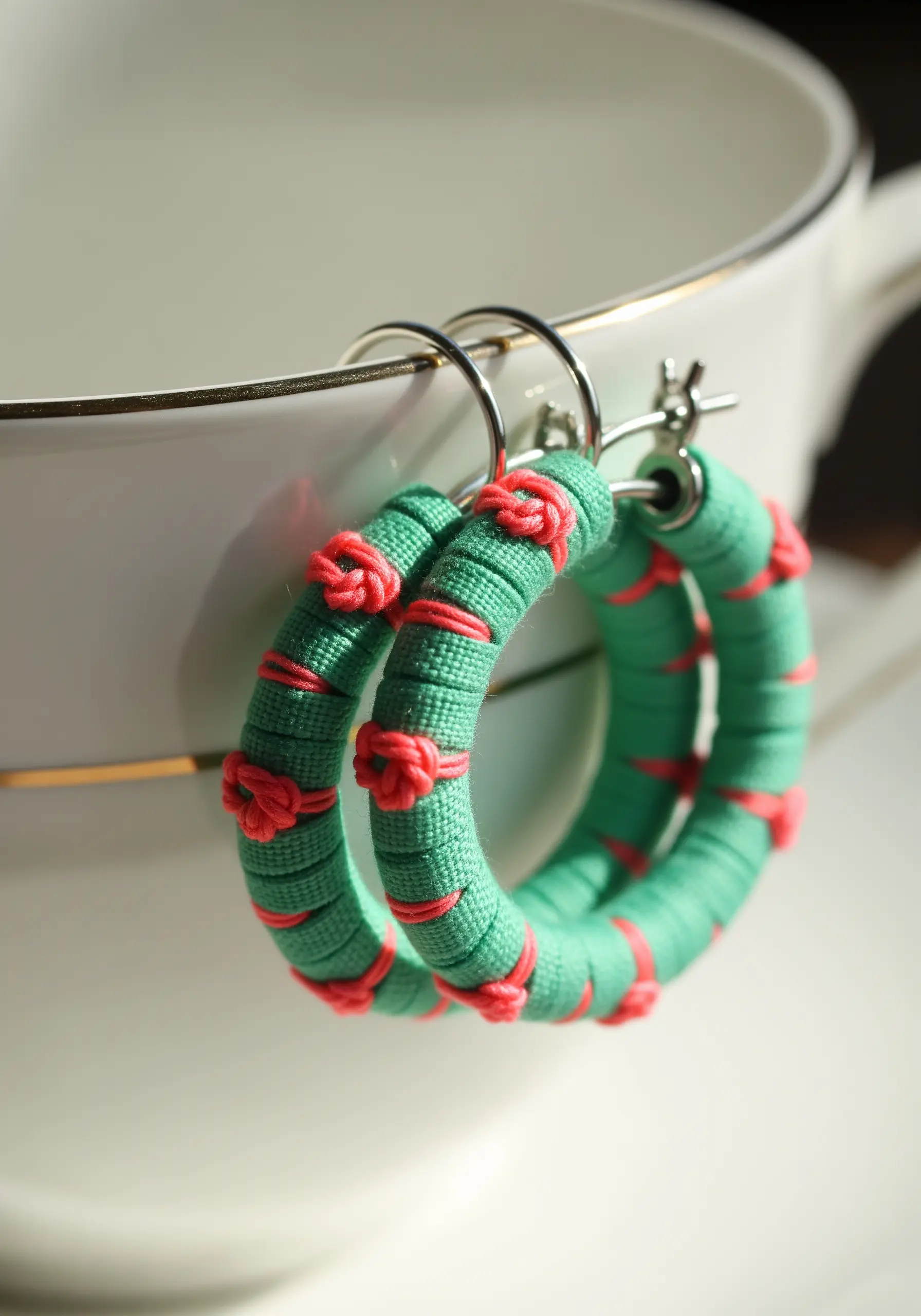 Green hoop earrings wrapped tightly with thread, with decorative pink knots tied over the top.