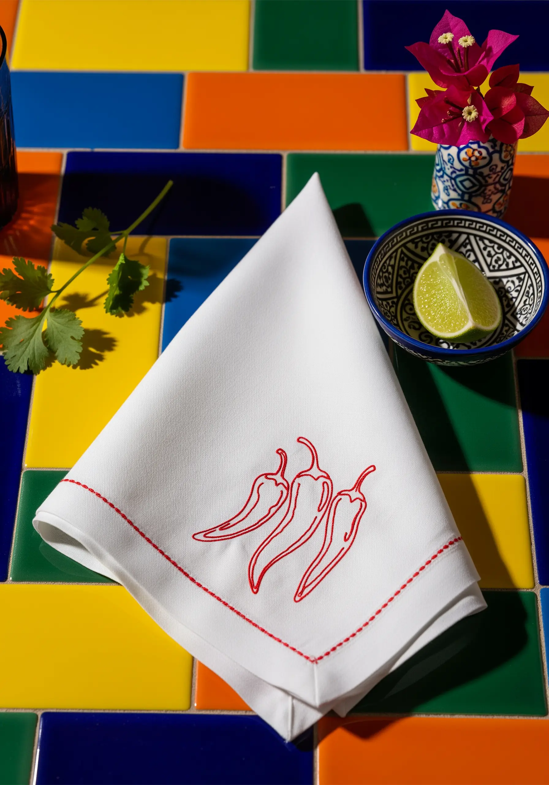 Three red chili peppers embroidered with a matching red border on a white napkin.