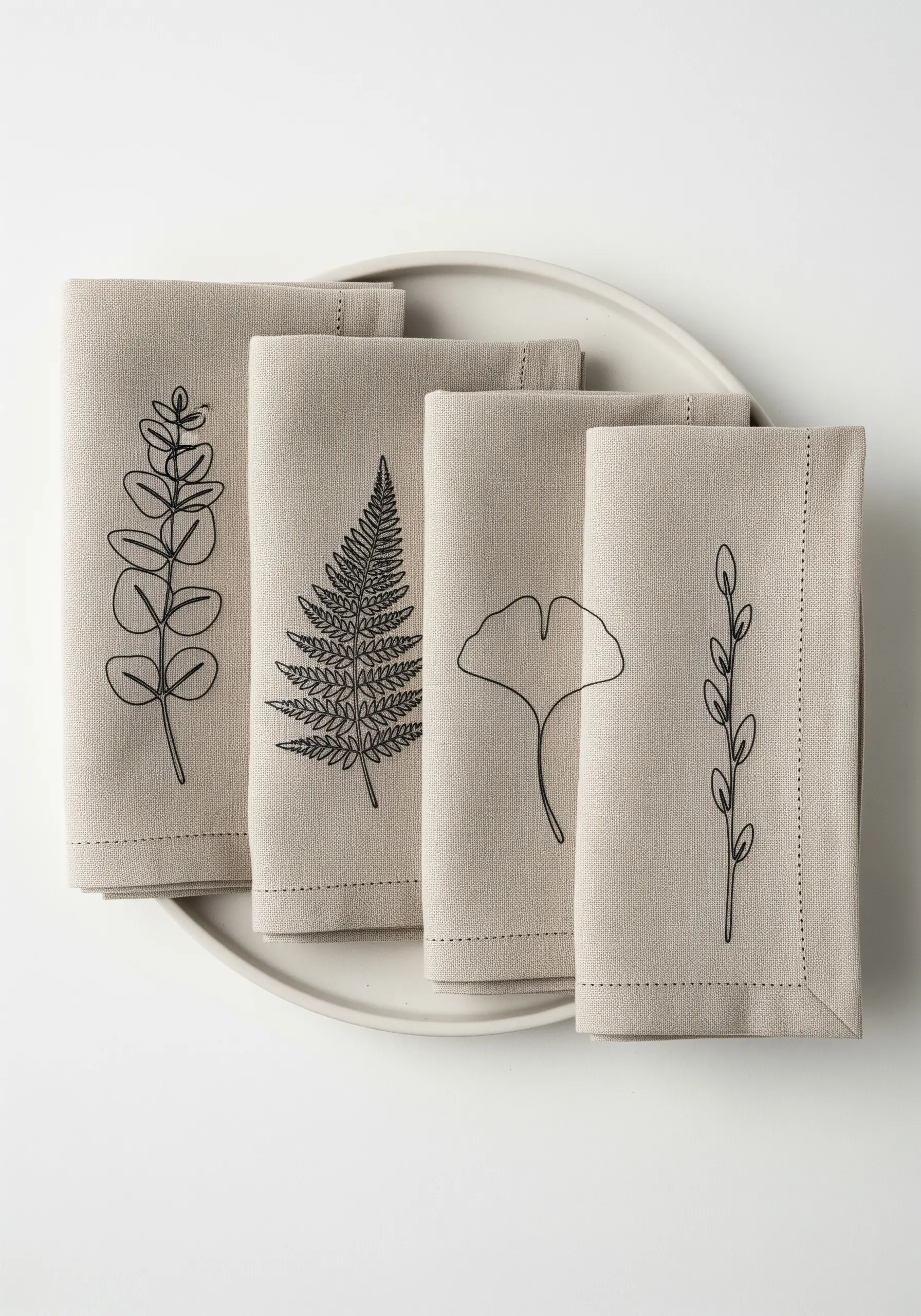 Four different one-line botanical motifs embroidered on folded linen napkins.