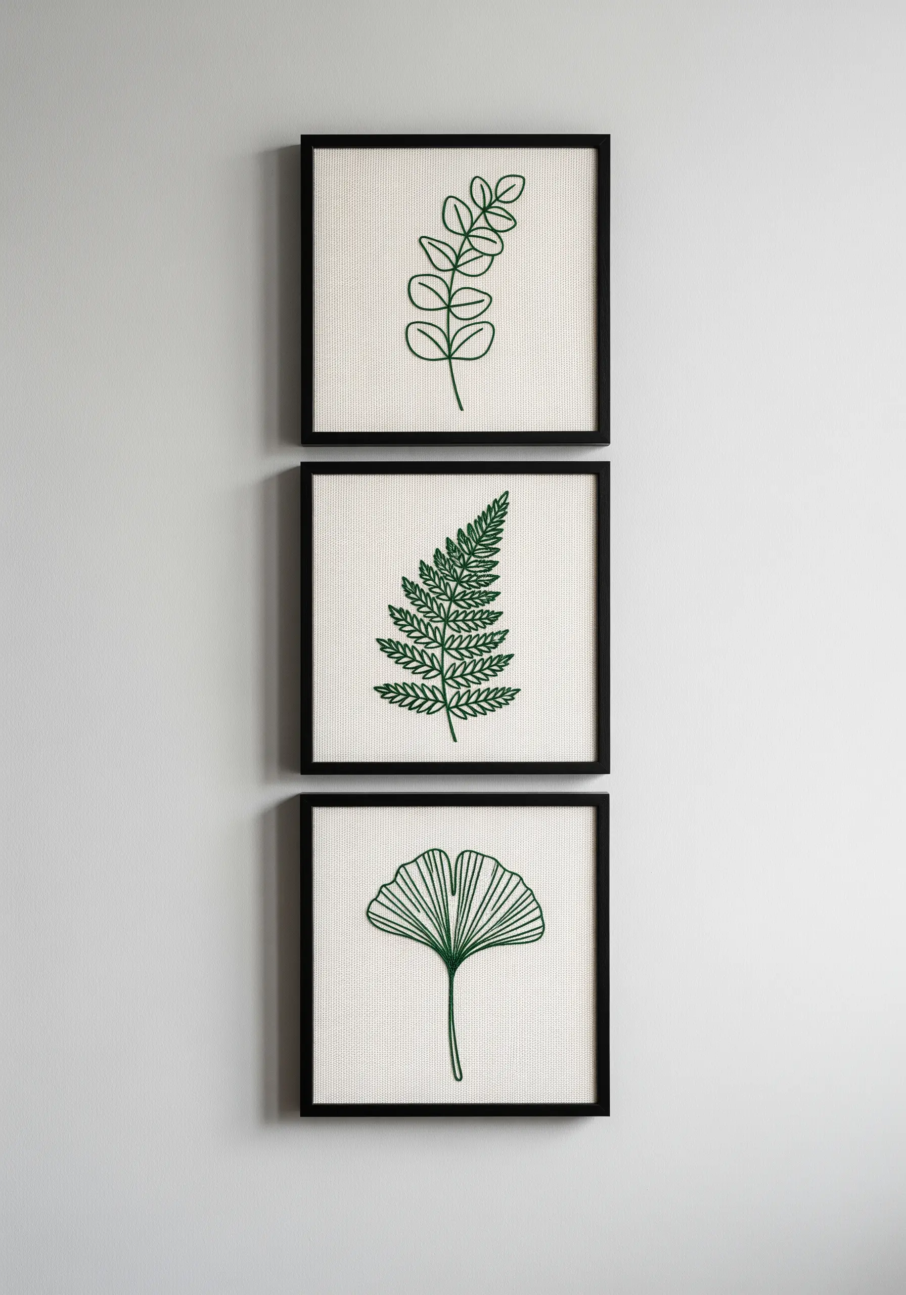 A set of three framed embroideries, each showing a different green leaf outline.