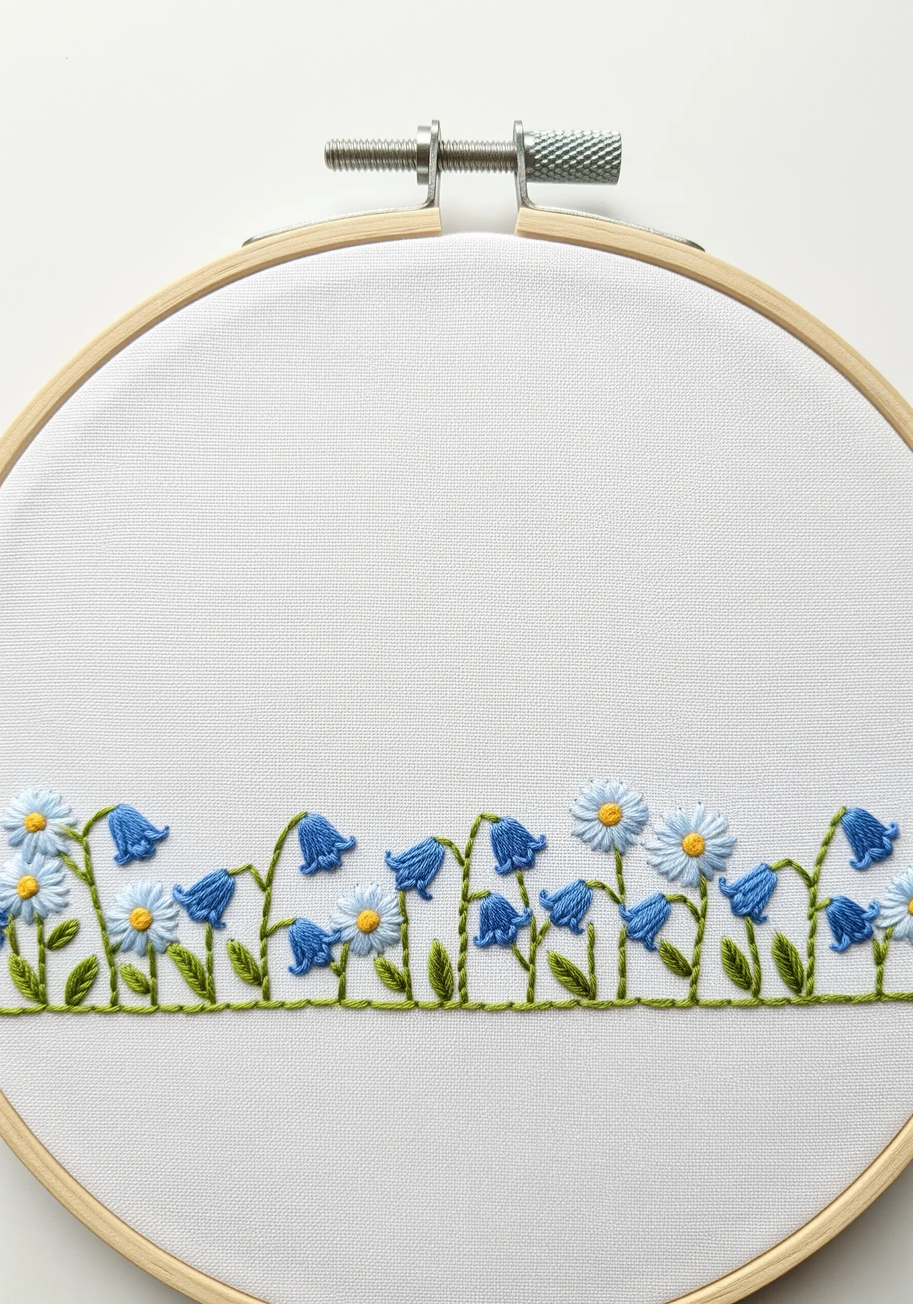 A border of embroidered wildflowers, including bluebells and daisies, along the bottom of a hoop.