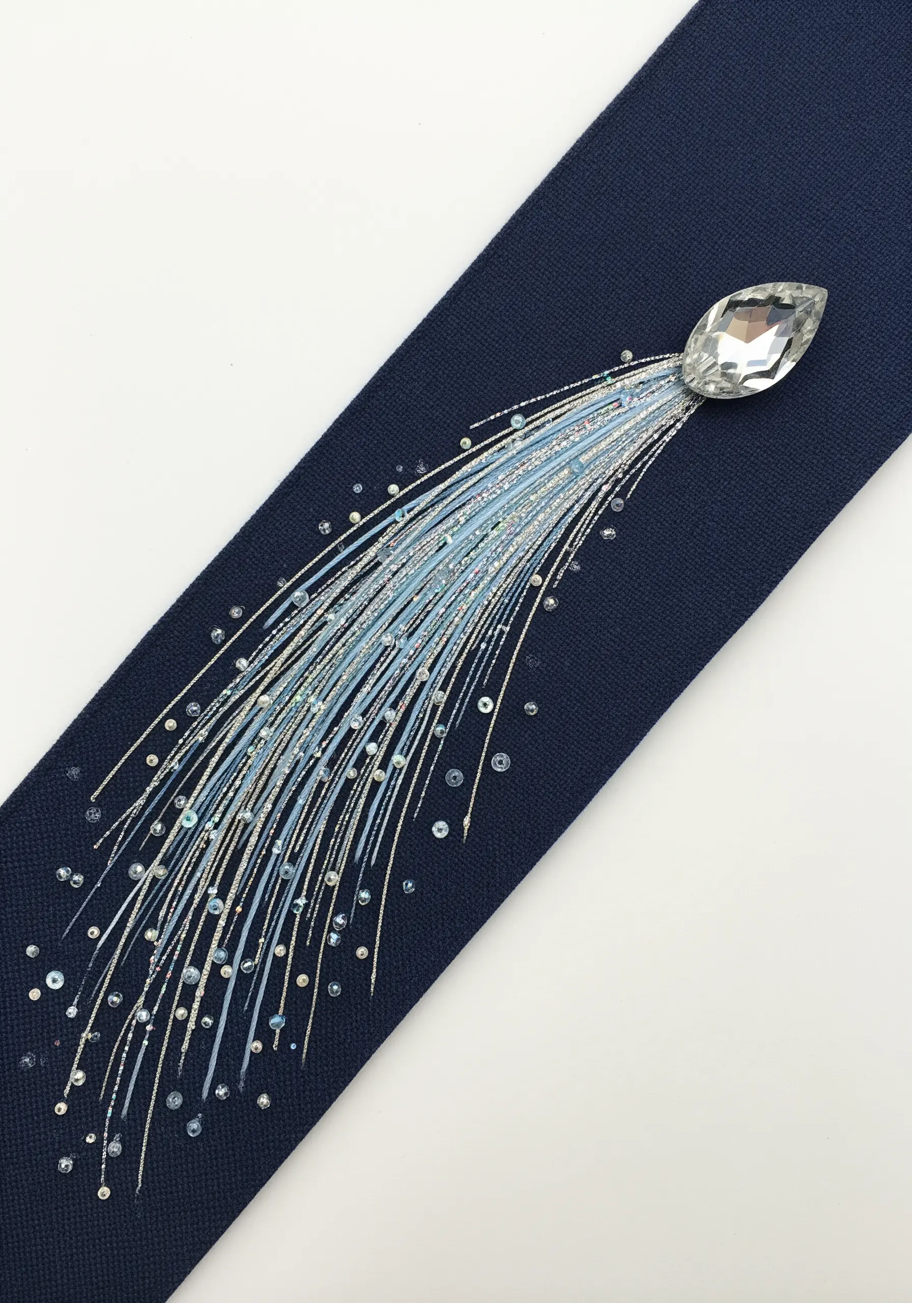 A large crystal bead with a tail of shimmering blue and silver threads and sequins.