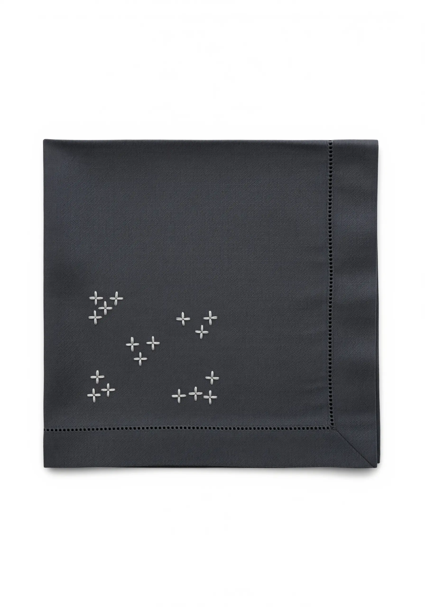 Scattered white cross stitches forming small constellations on a dark grey napkin.