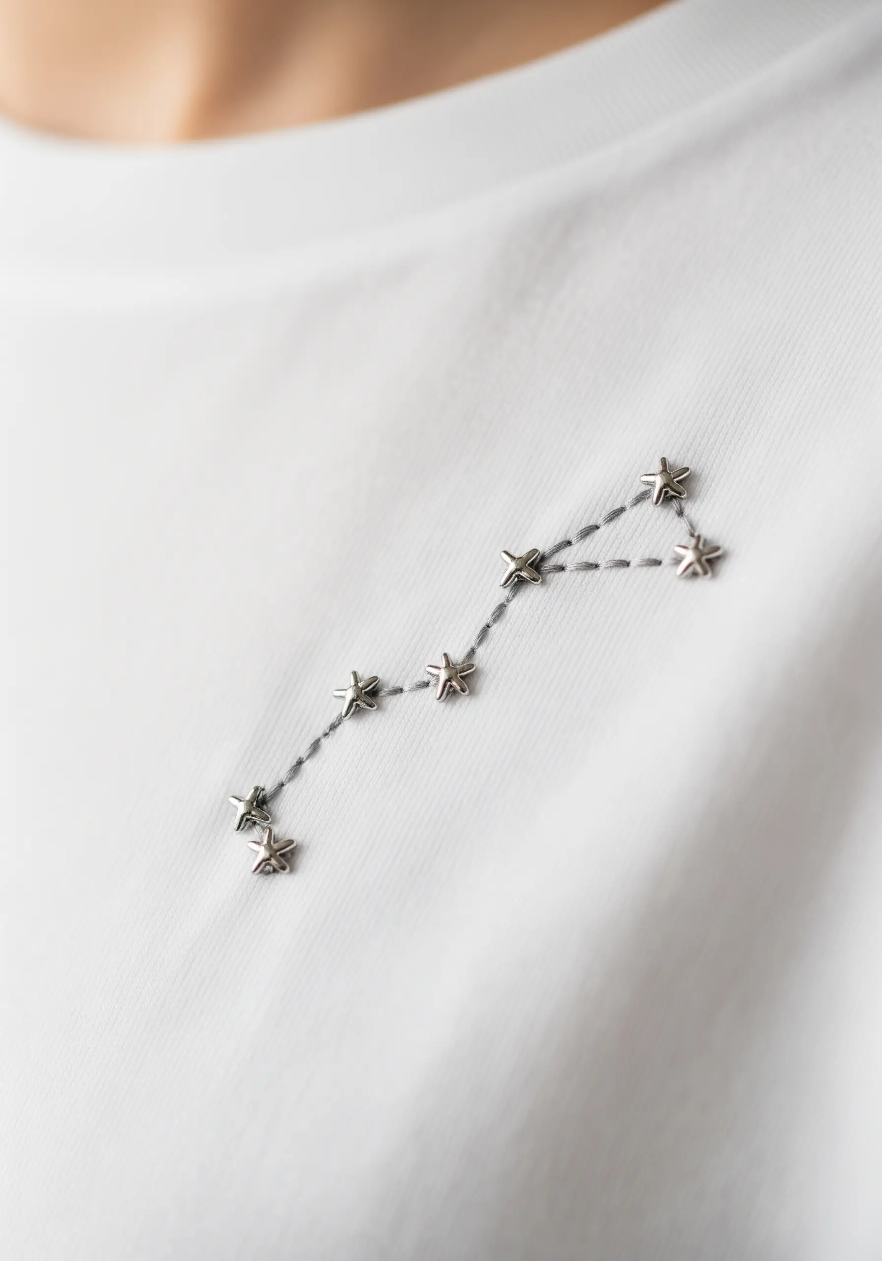 A constellation embroidered with grey thread and small silver star studs.