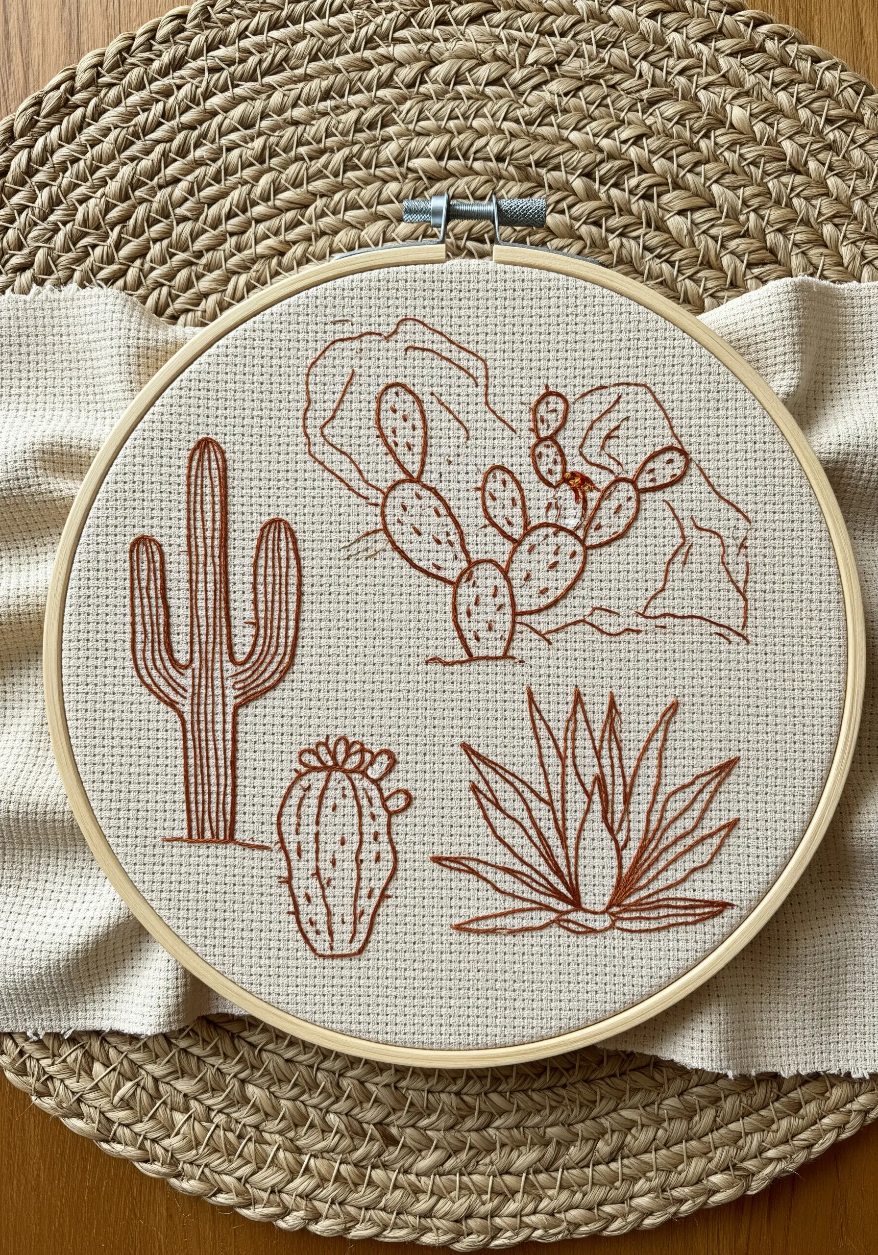 A collection of desert cacti and plants embroidered in terracotta-colored thread on Aida cloth.