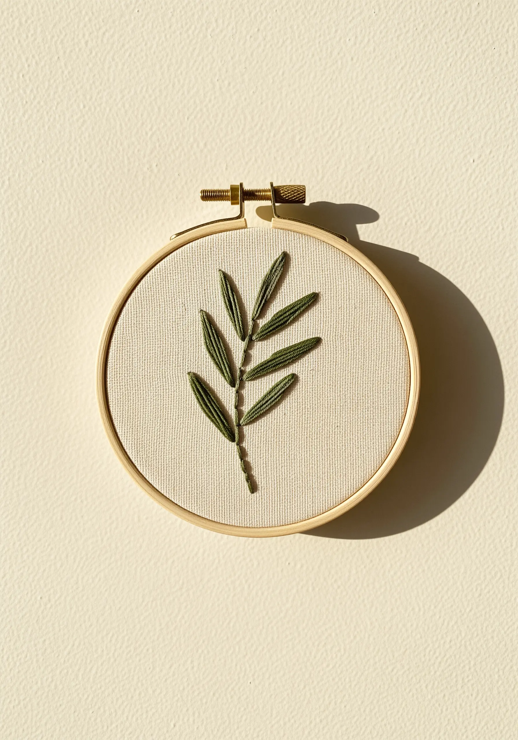 A single olive branch with satin-stitched green leaves embroidered in a small hoop.