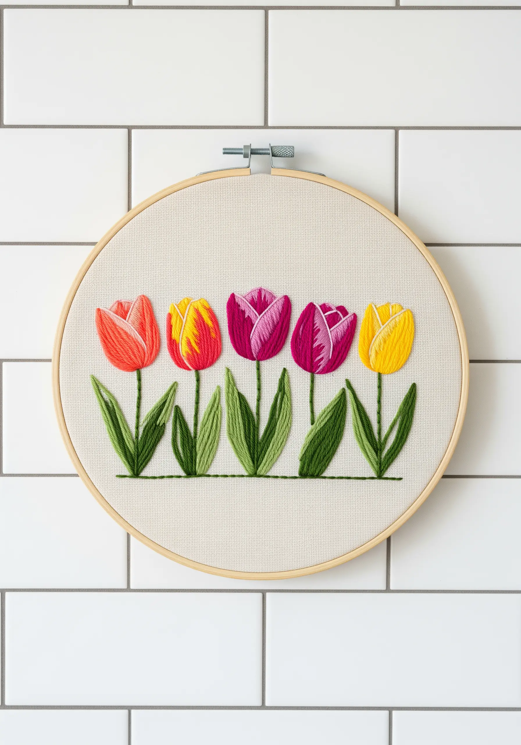 A row of five colorful tulips with blended satin stitch against a white tiled wall.
