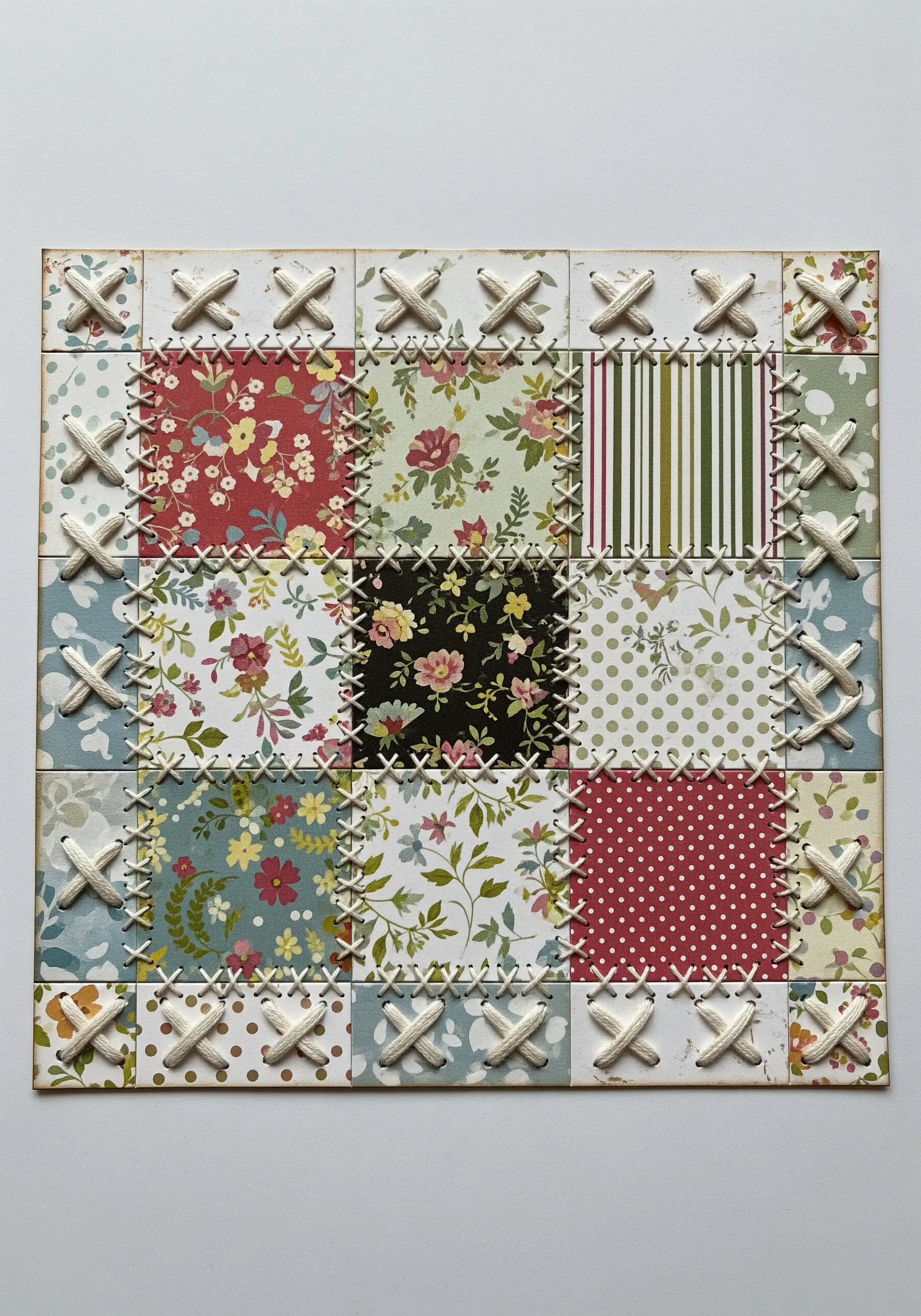 A grid of patterned paper squares stitched together with thick, white yarn in cross-stitches.