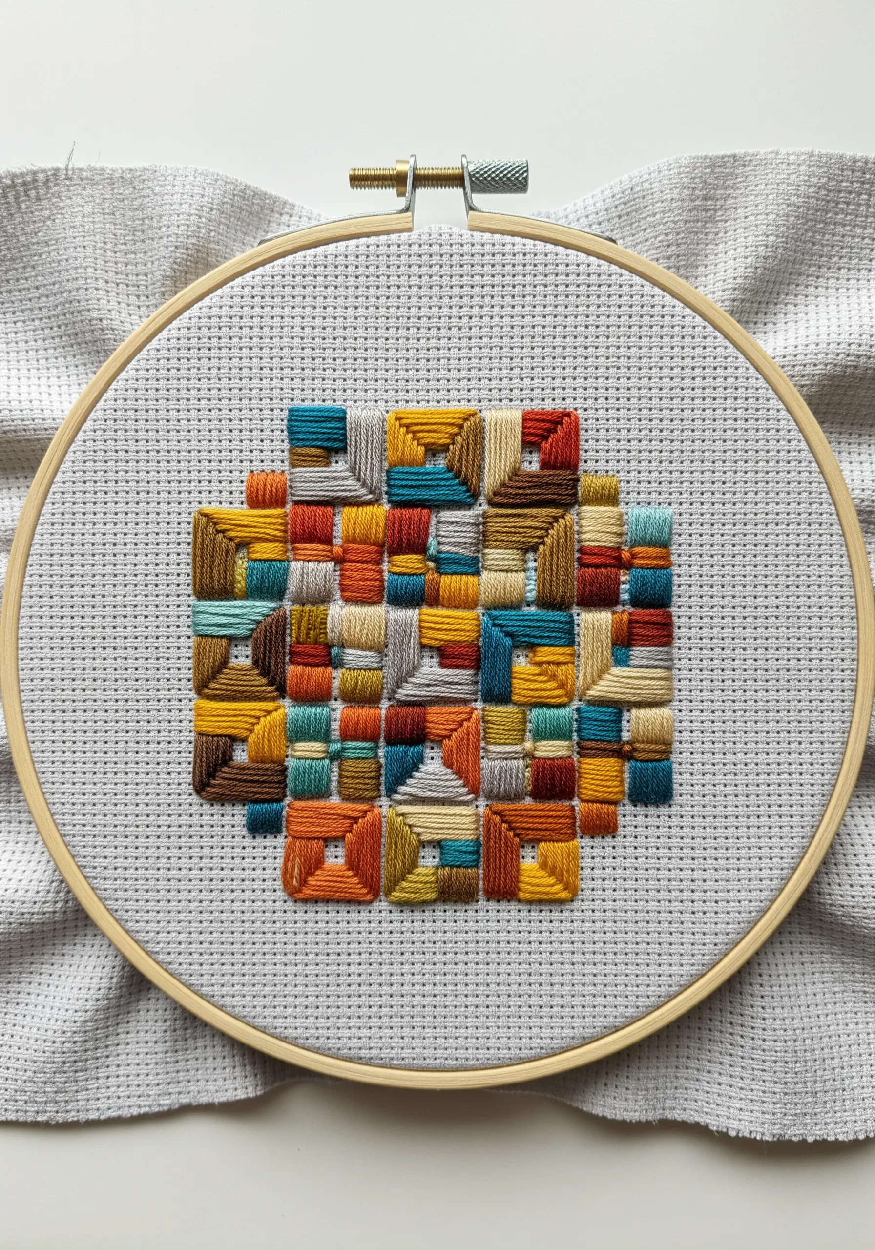 A geometric patchwork of small squares filled with satin stitch in multiple directions.