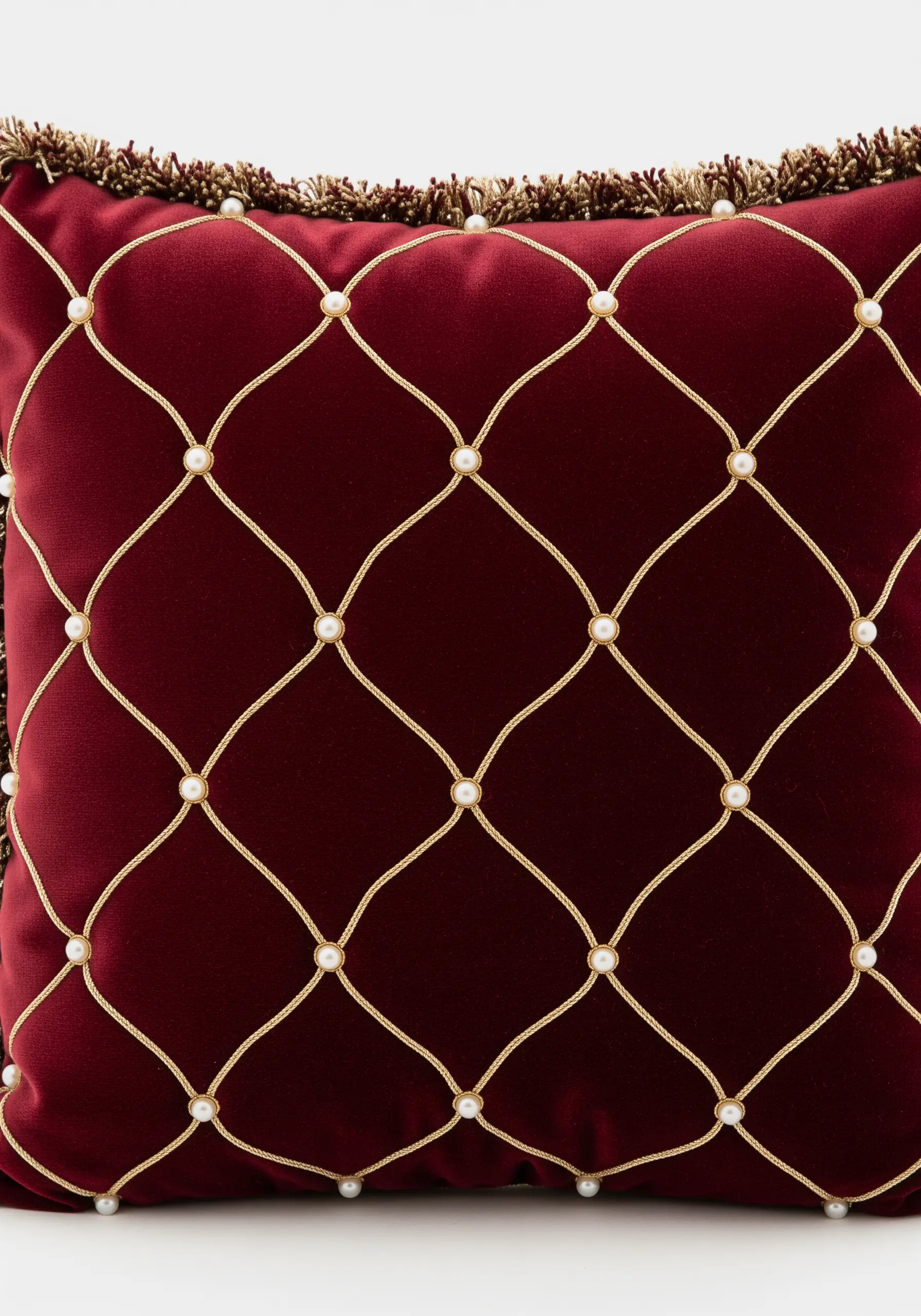 A gold cord trellis pattern accented with pearls on a rich red velvet cushion.