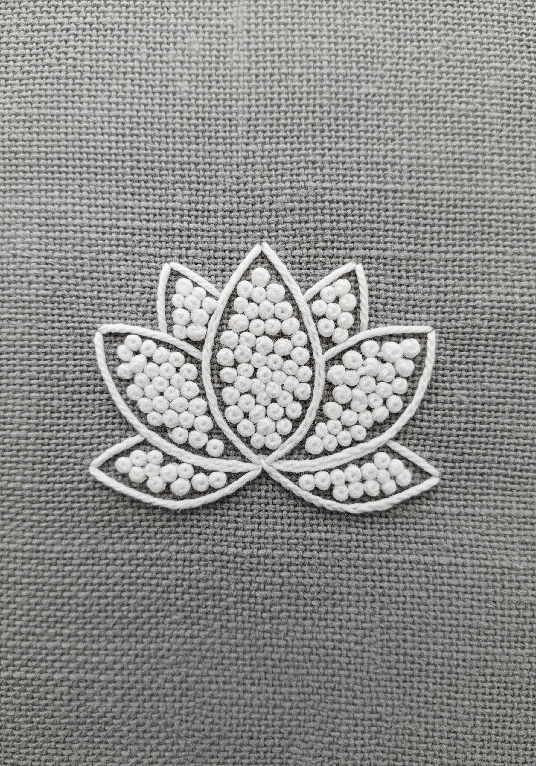 A lotus flower outlined in white and filled entirely with white French knots on grey fabric.