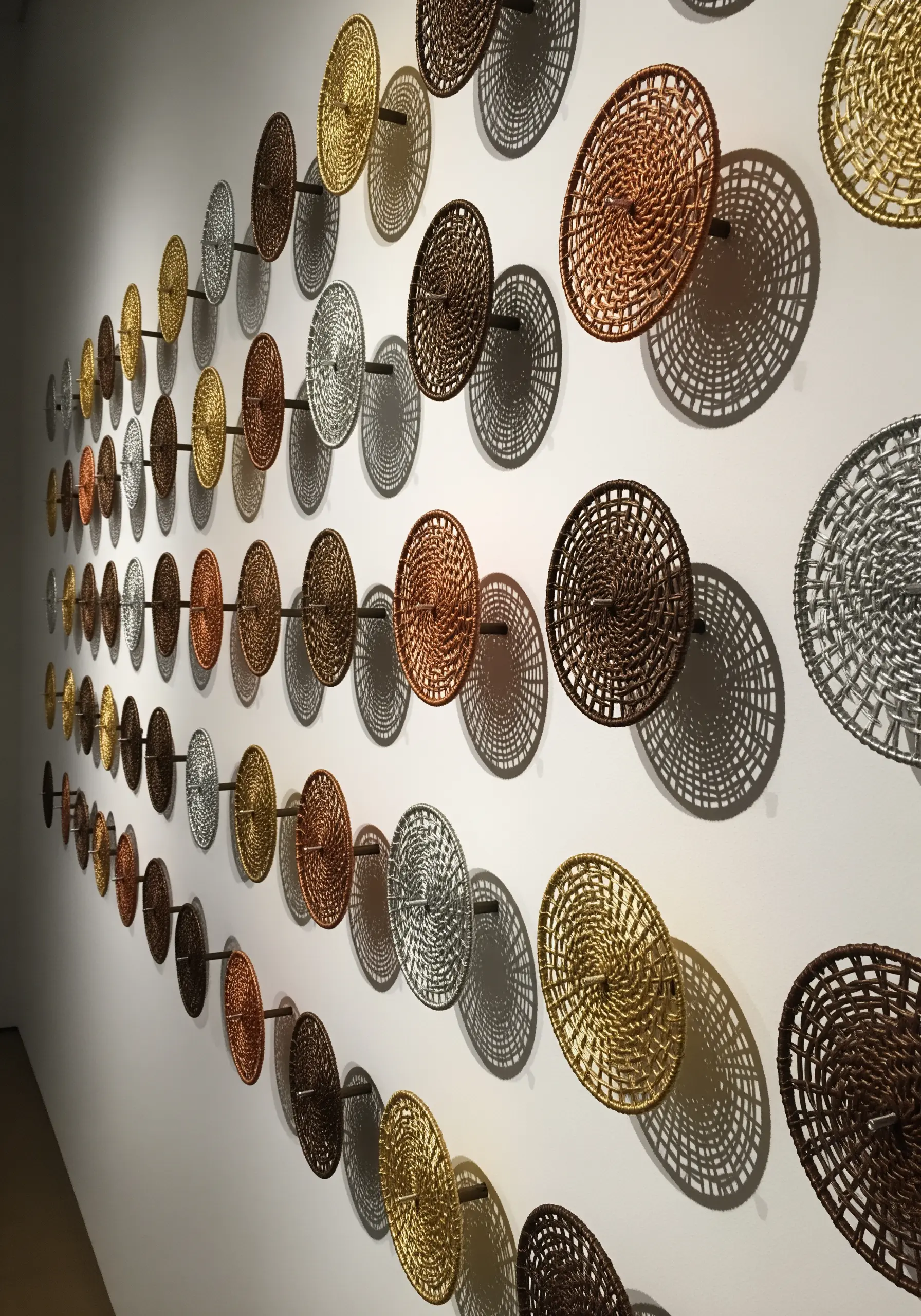 A wall installation of many small, woven metallic discs mounted on posts.