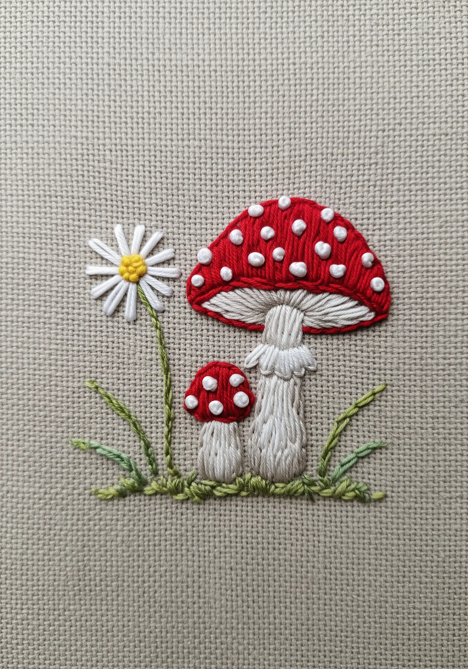 An embroidered red toadstool mushroom with white spots, next to a small daisy.