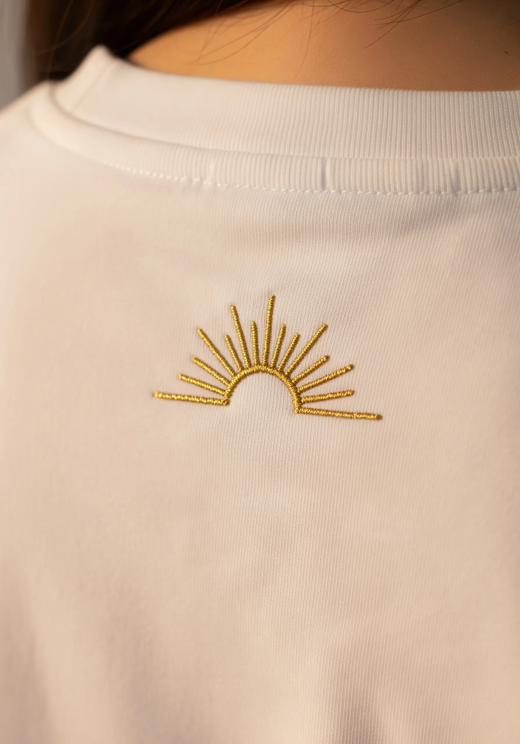A minimal rising sun motif in gold metallic thread on the back of a t-shirt.