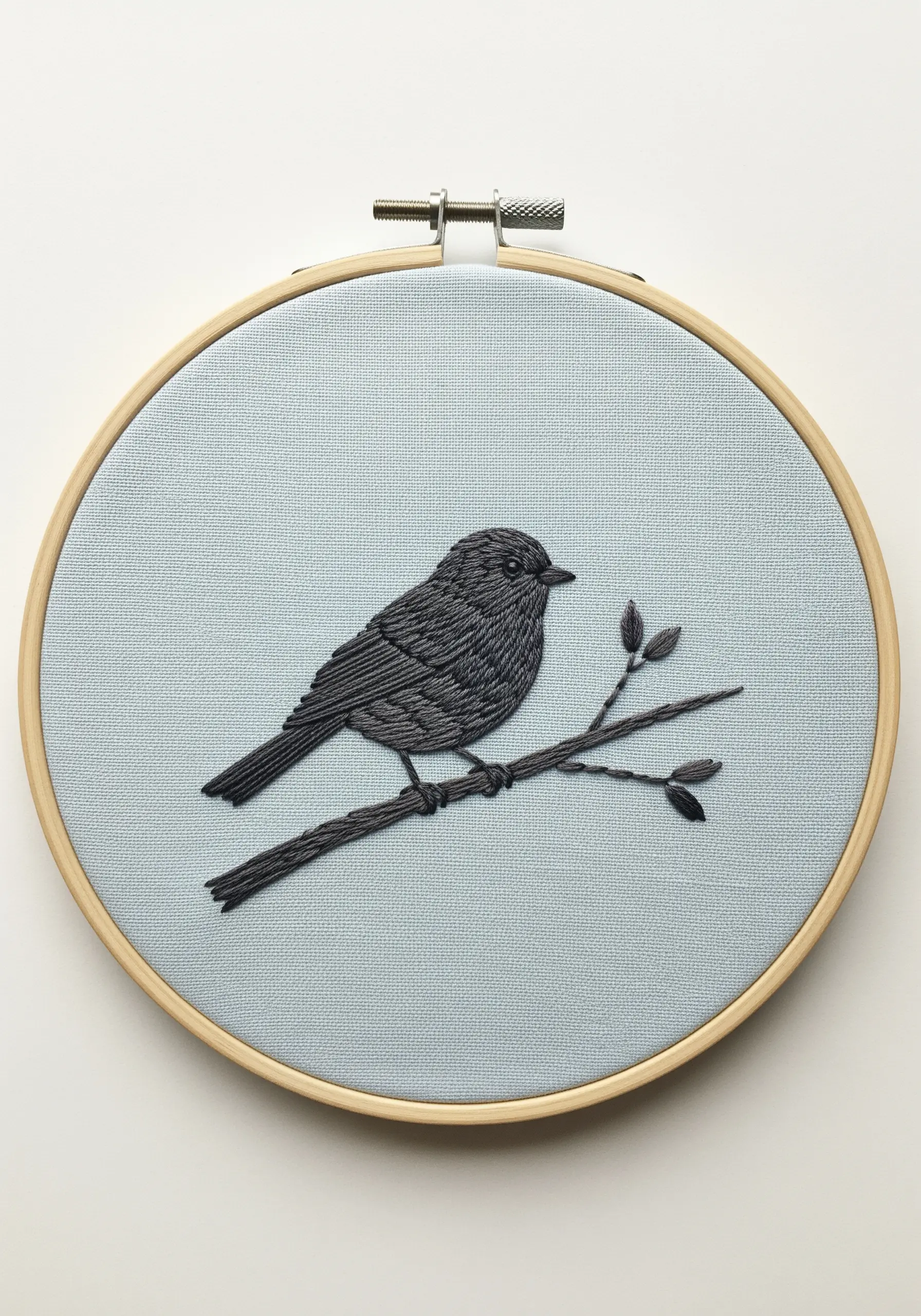 A small bird on a branch embroidered in shades of gray on blue fabric.