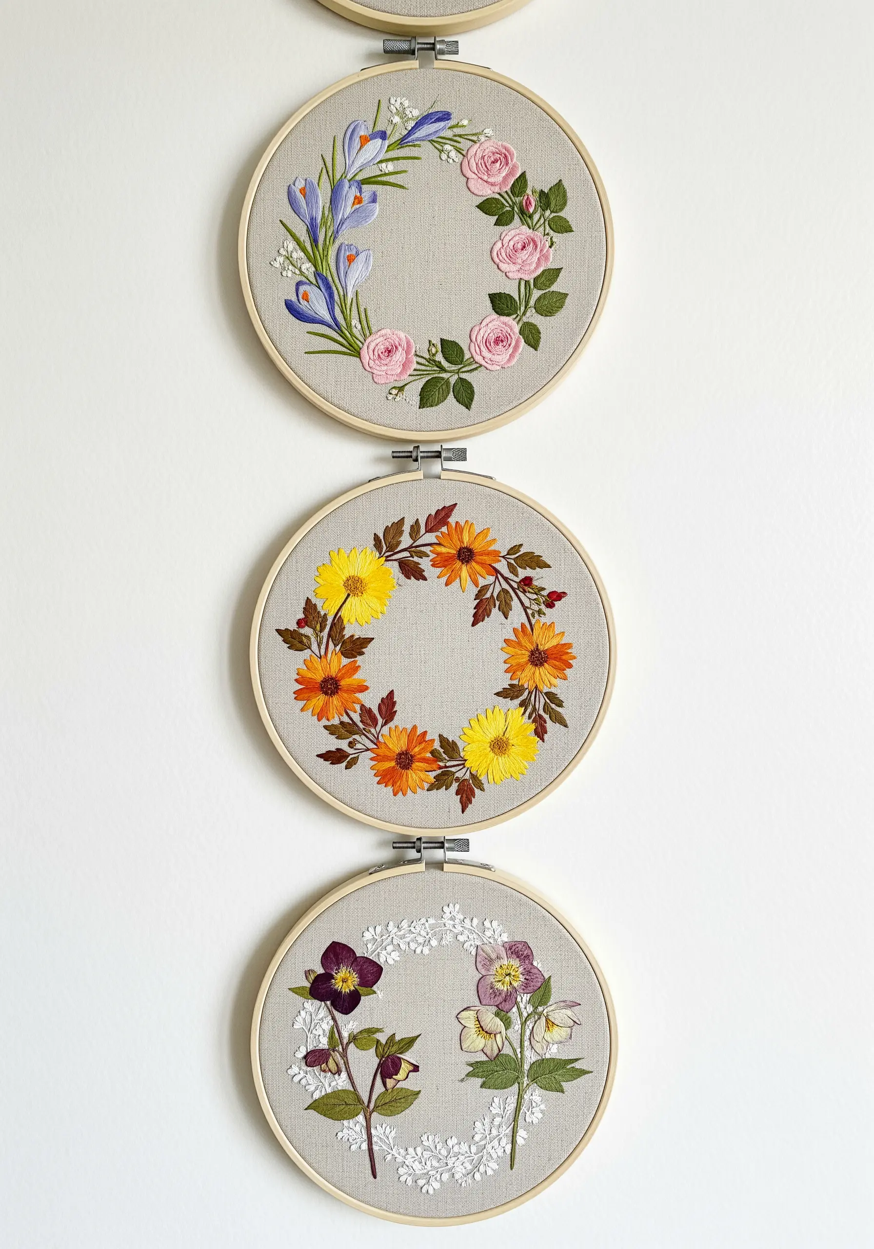 Three embroidery hoops hung vertically, each containing a different seasonal floral wreath design.