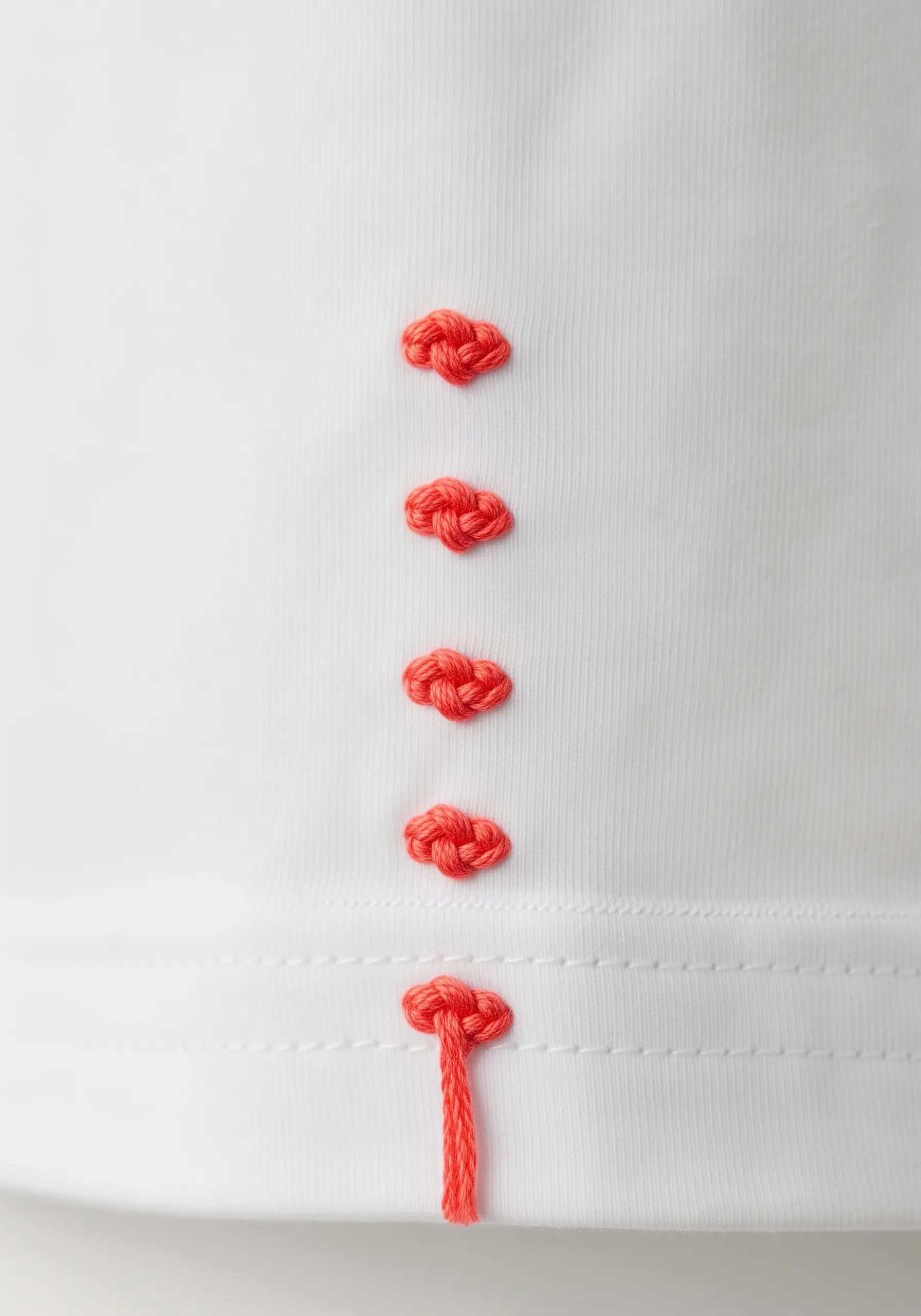 A vertical row of five textured, coral-colored embroidered knots.