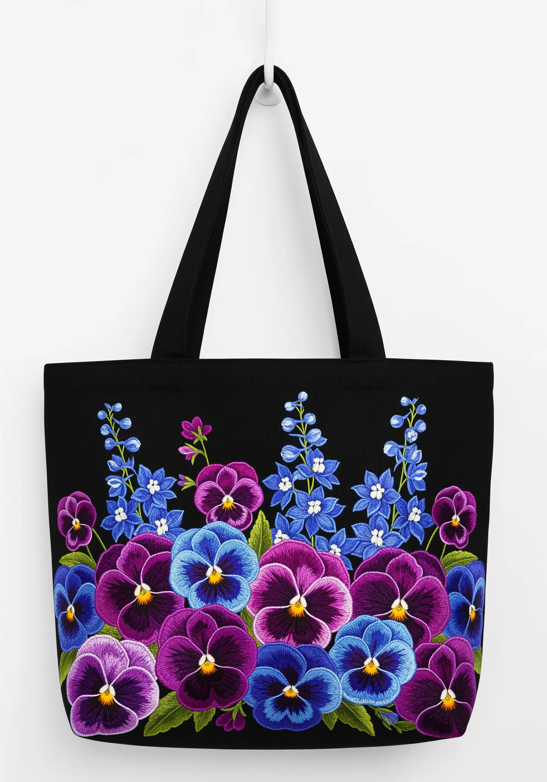 A dense border of embroidered pansies in purple and blue on a black tote bag.