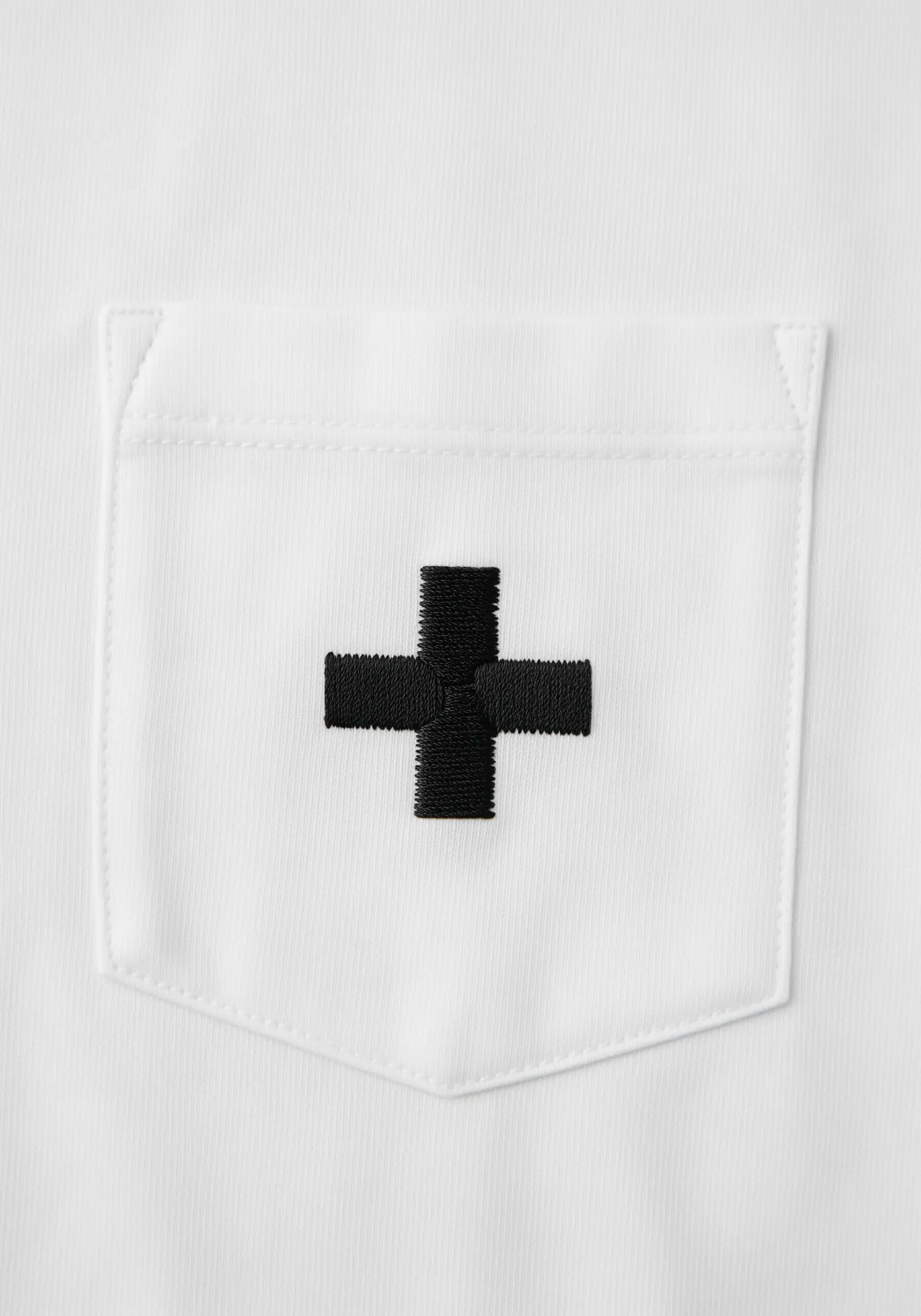 A thick, woven black plus sign embroidered on a t-shirt pocket.
