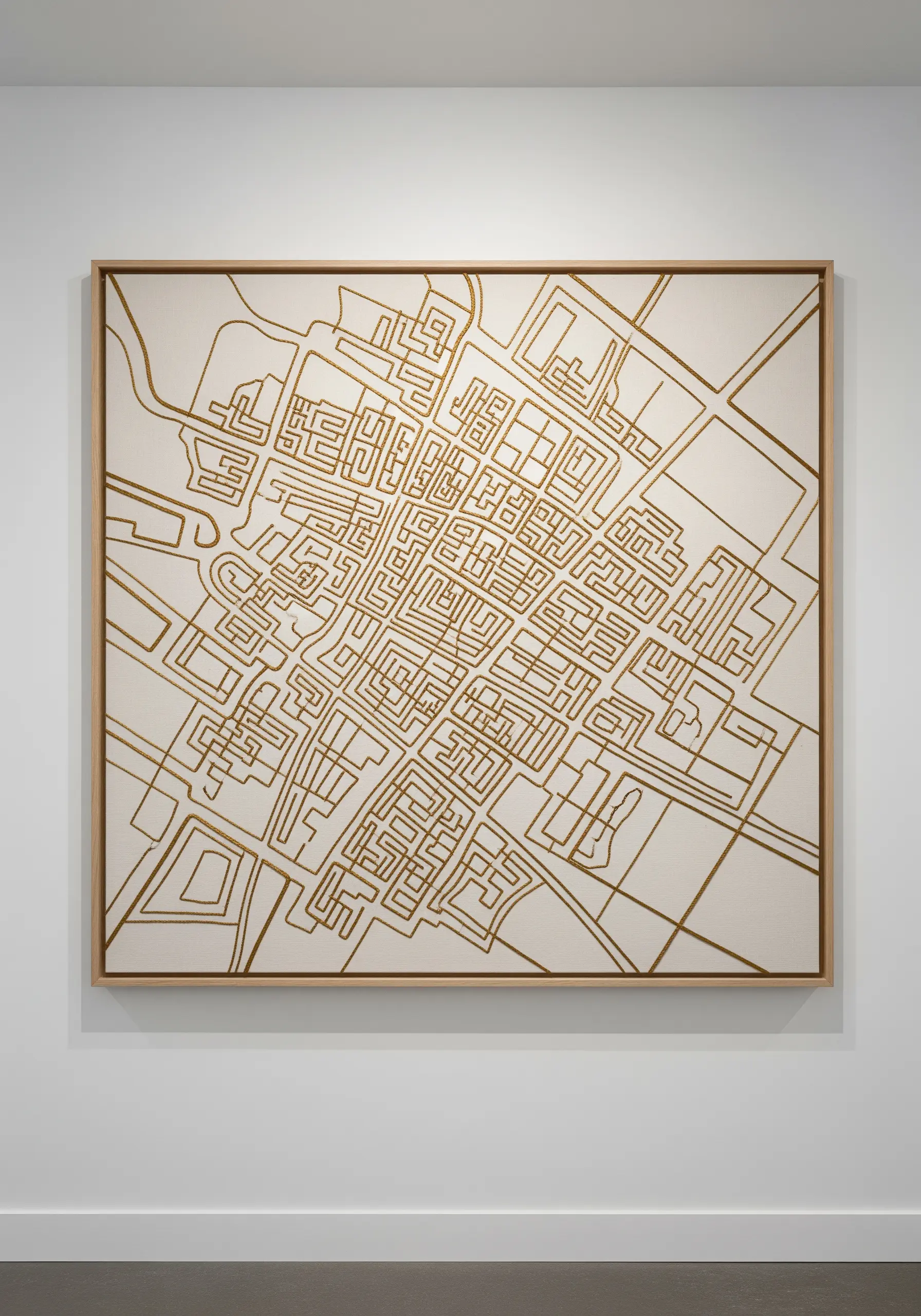 An abstract city map embroidered in gold thread on a large off-white canvas.