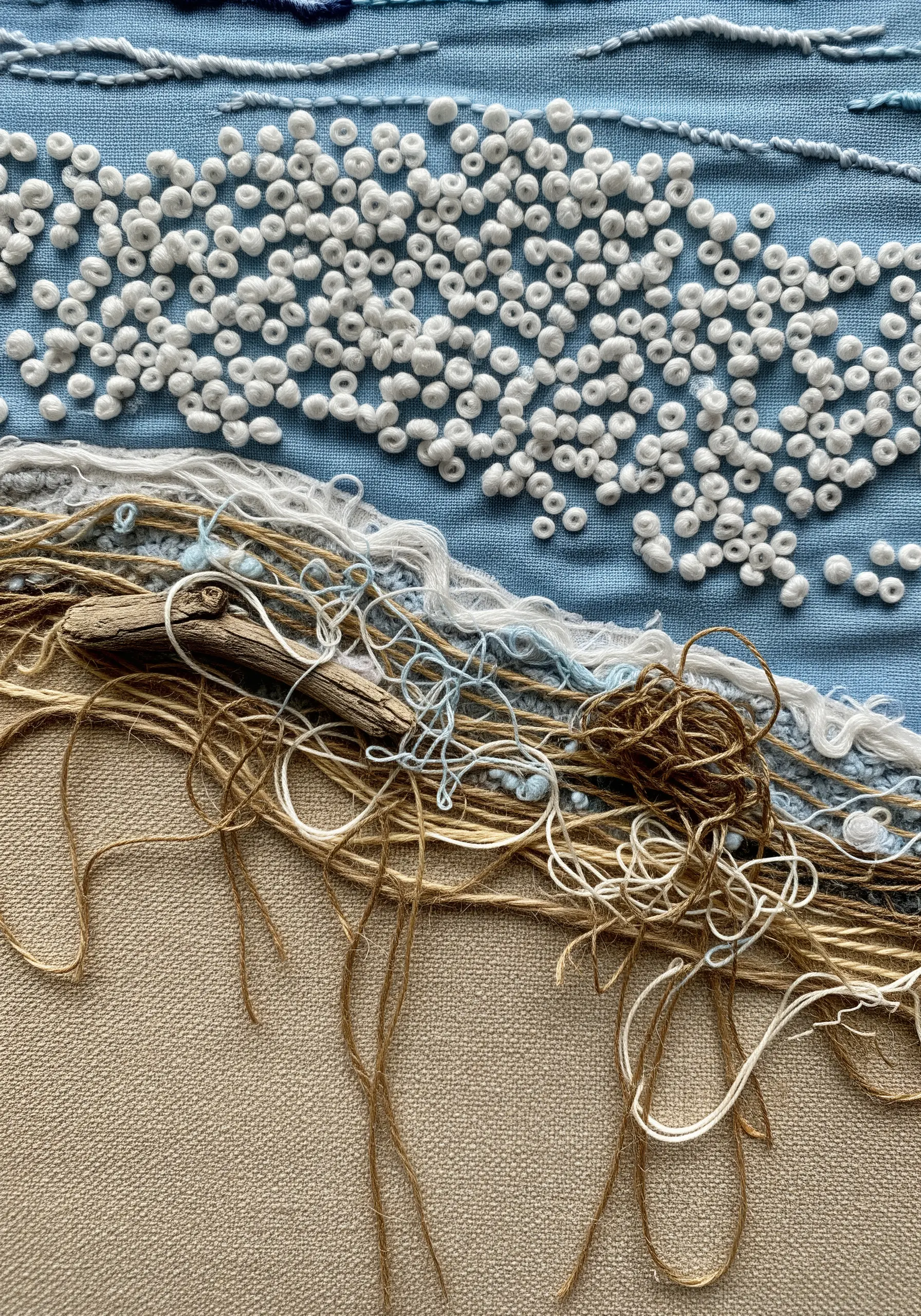Abstract coastal embroidery with driftwood, jute, and white knots on blue and beige fabric.
