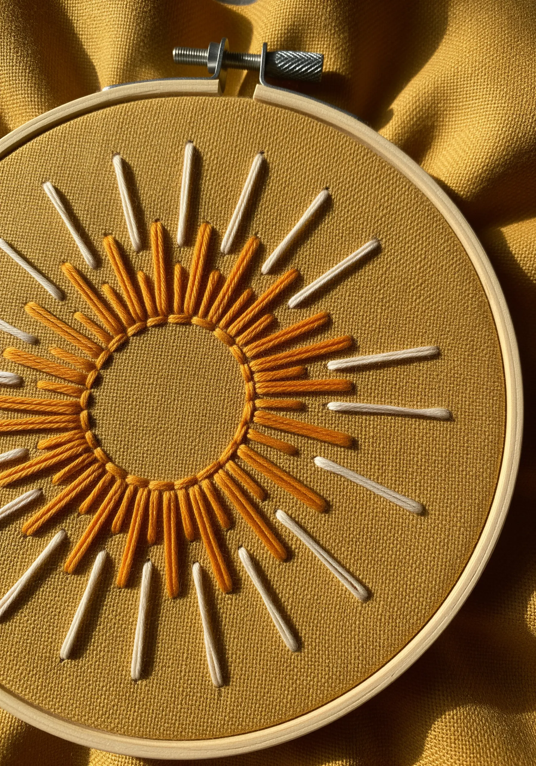 Abstract sun stitched with radiating orange and cream straight stitches on yellow fabric.
