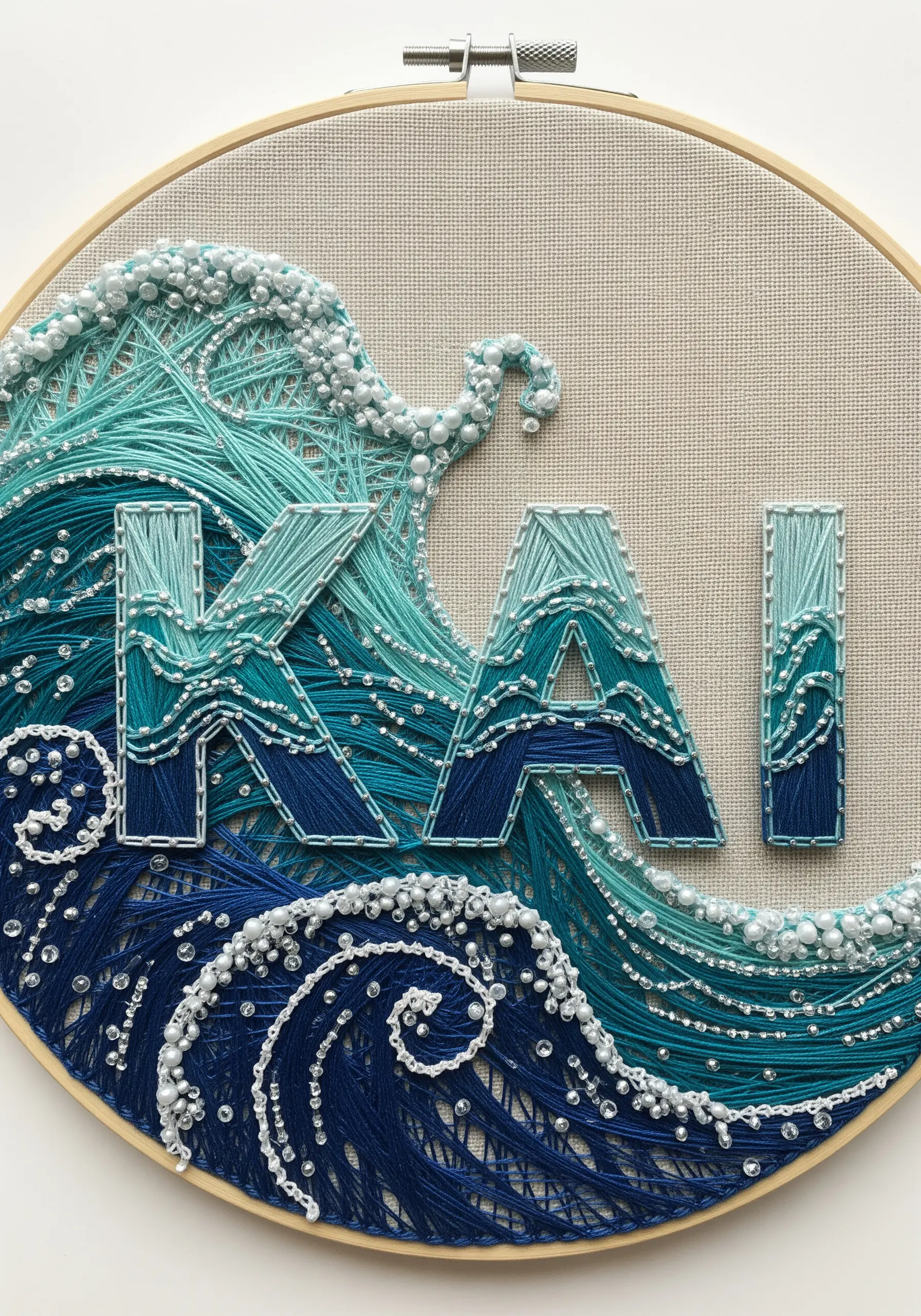 Embroidered name integrated into a textured ocean wave using French knots and beads.