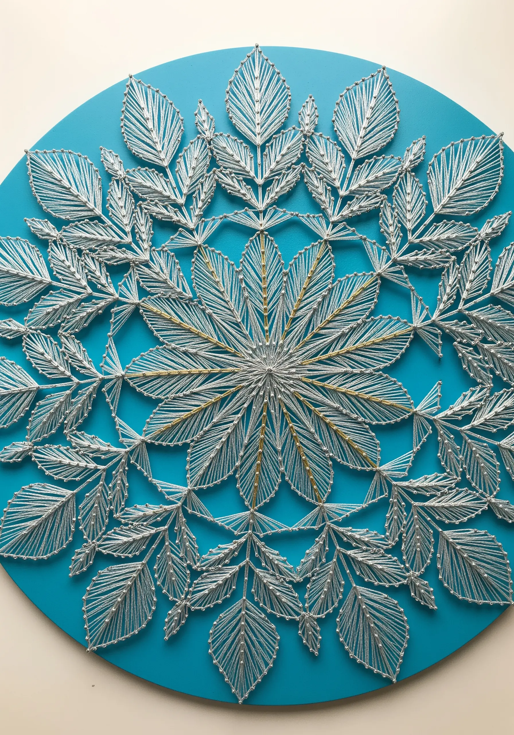A string art mandala made of silver leaves on a blue background, with central gold accents.