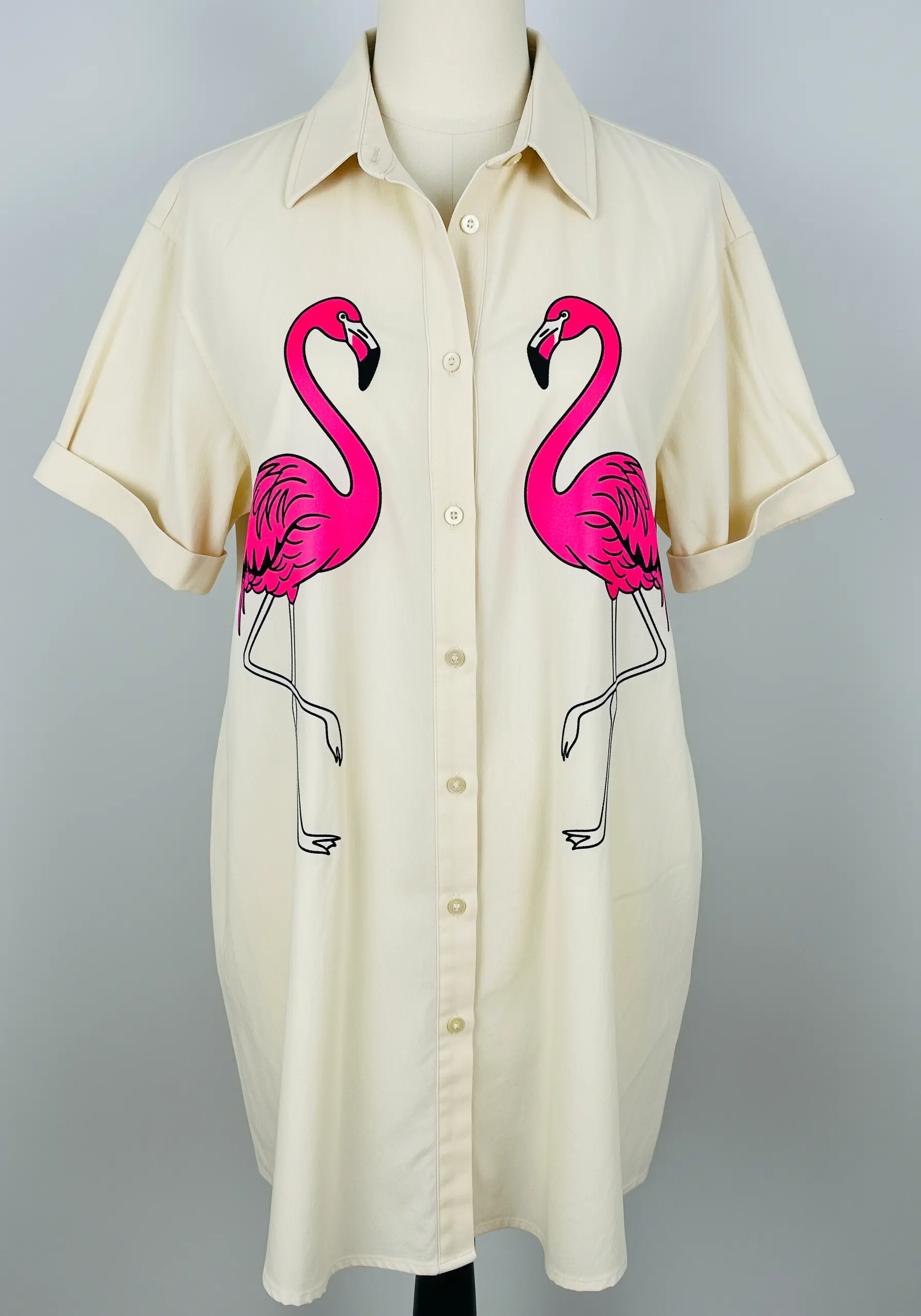Two bright pink pop-art style flamingos on a cream-colored shirt dress with black outlines.