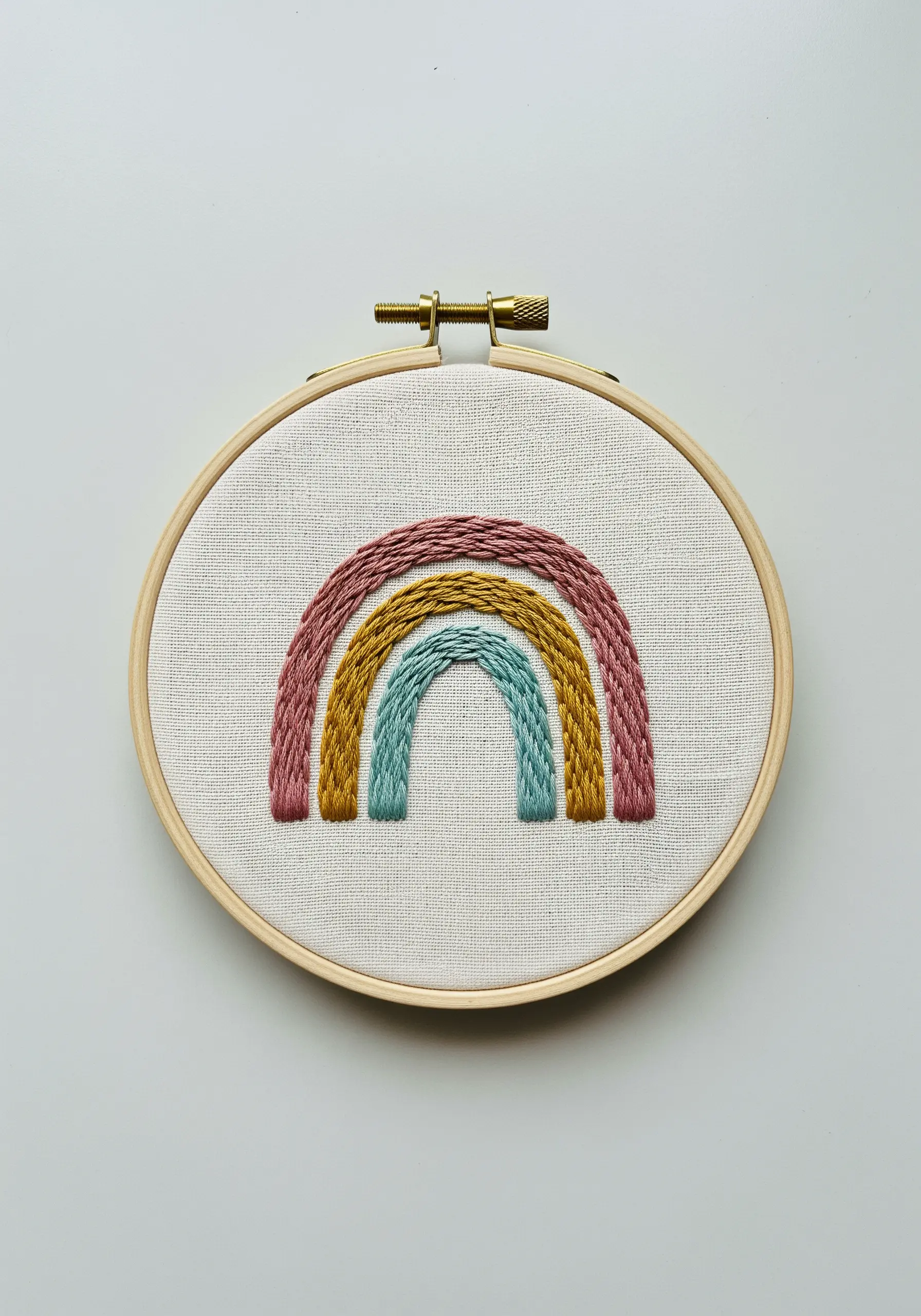 A small, textured rainbow with three arches in muted colors, stitched with chain stitch.