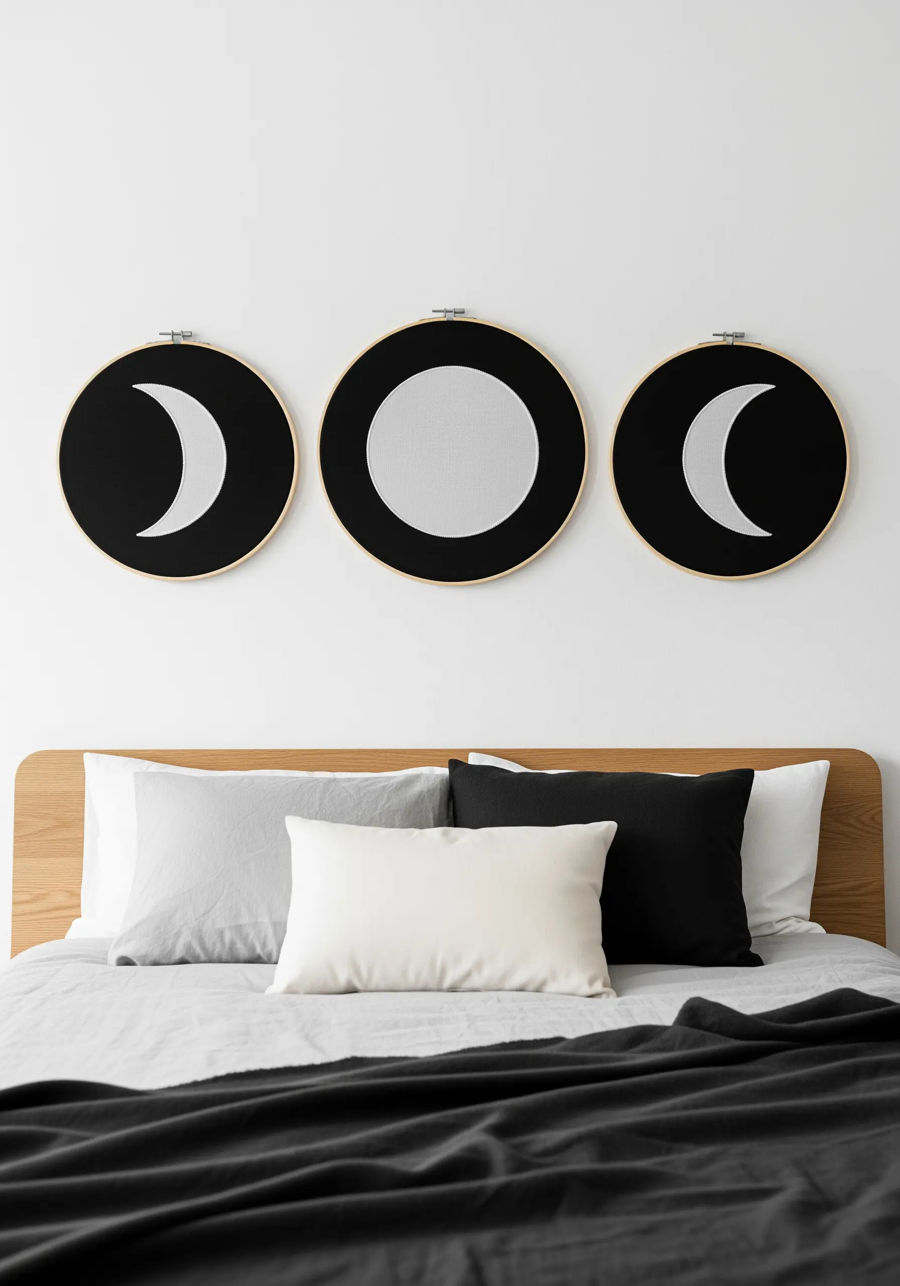 A triptych of moon phase embroidery in black and white hanging above a bed.