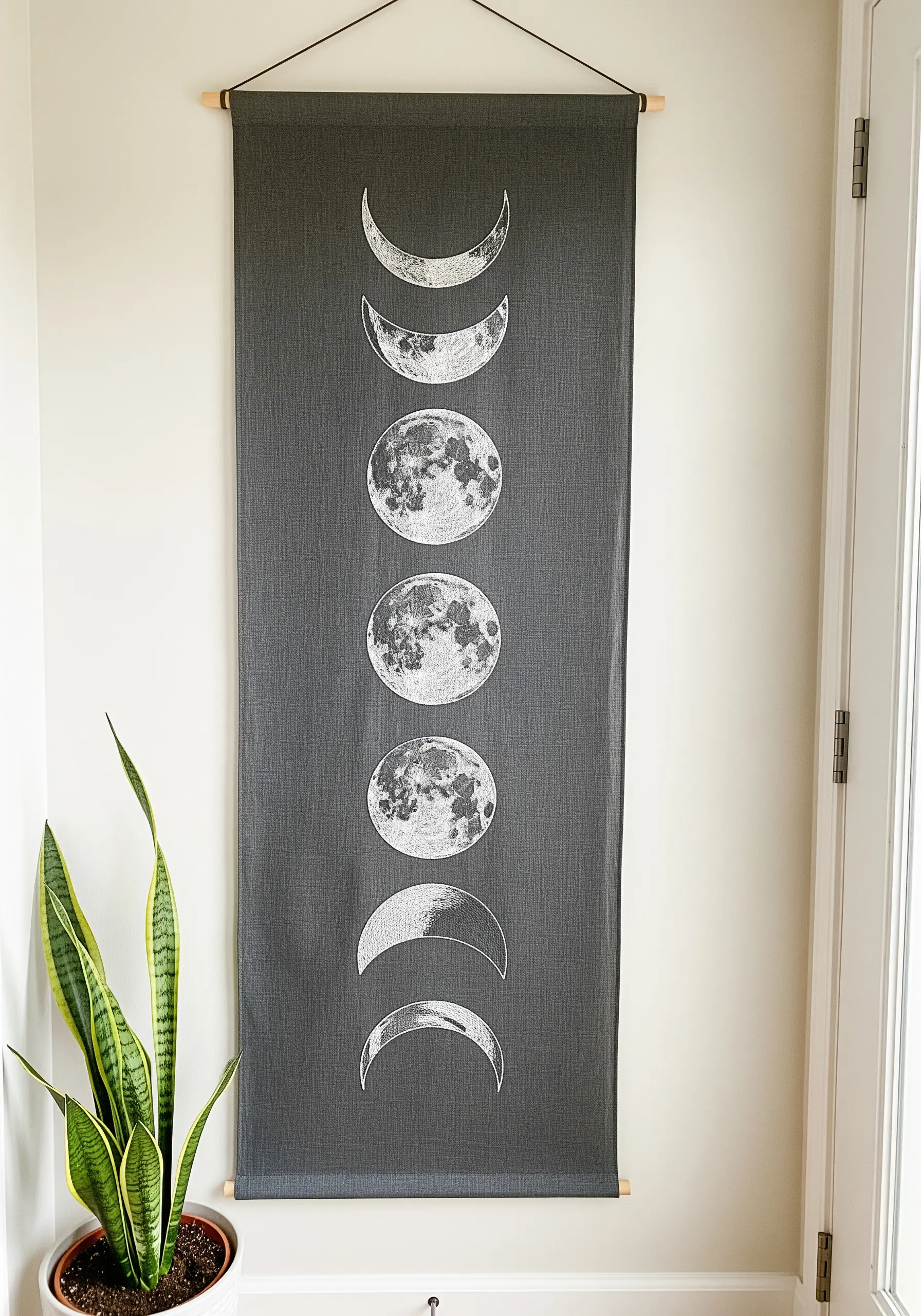 A long, dark grey wall hanging displaying the phases of the moon in white thread.
