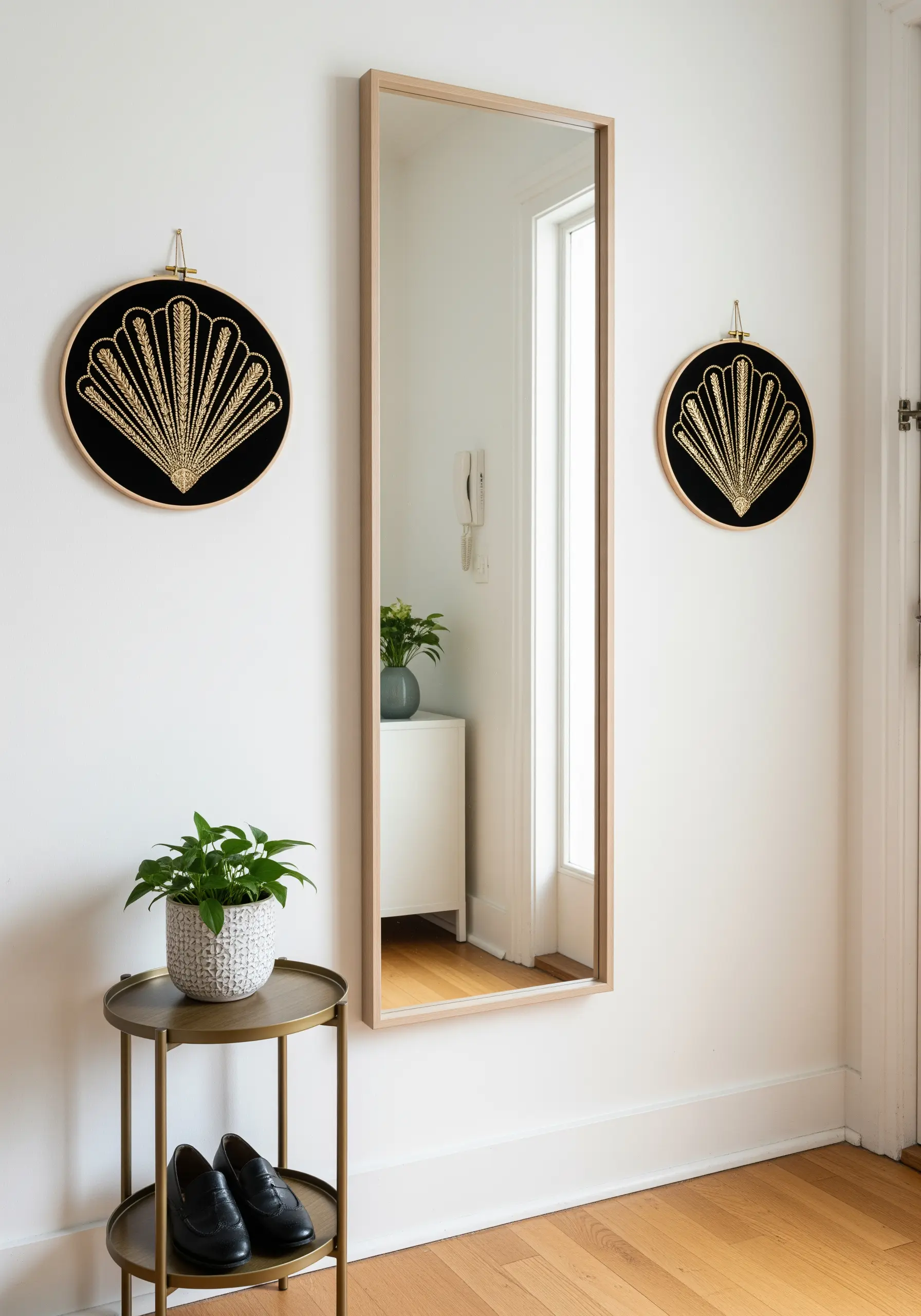 Two identical embroidery hoops with gold metallic Art Deco fan designs on black fabric flanking a mirror.