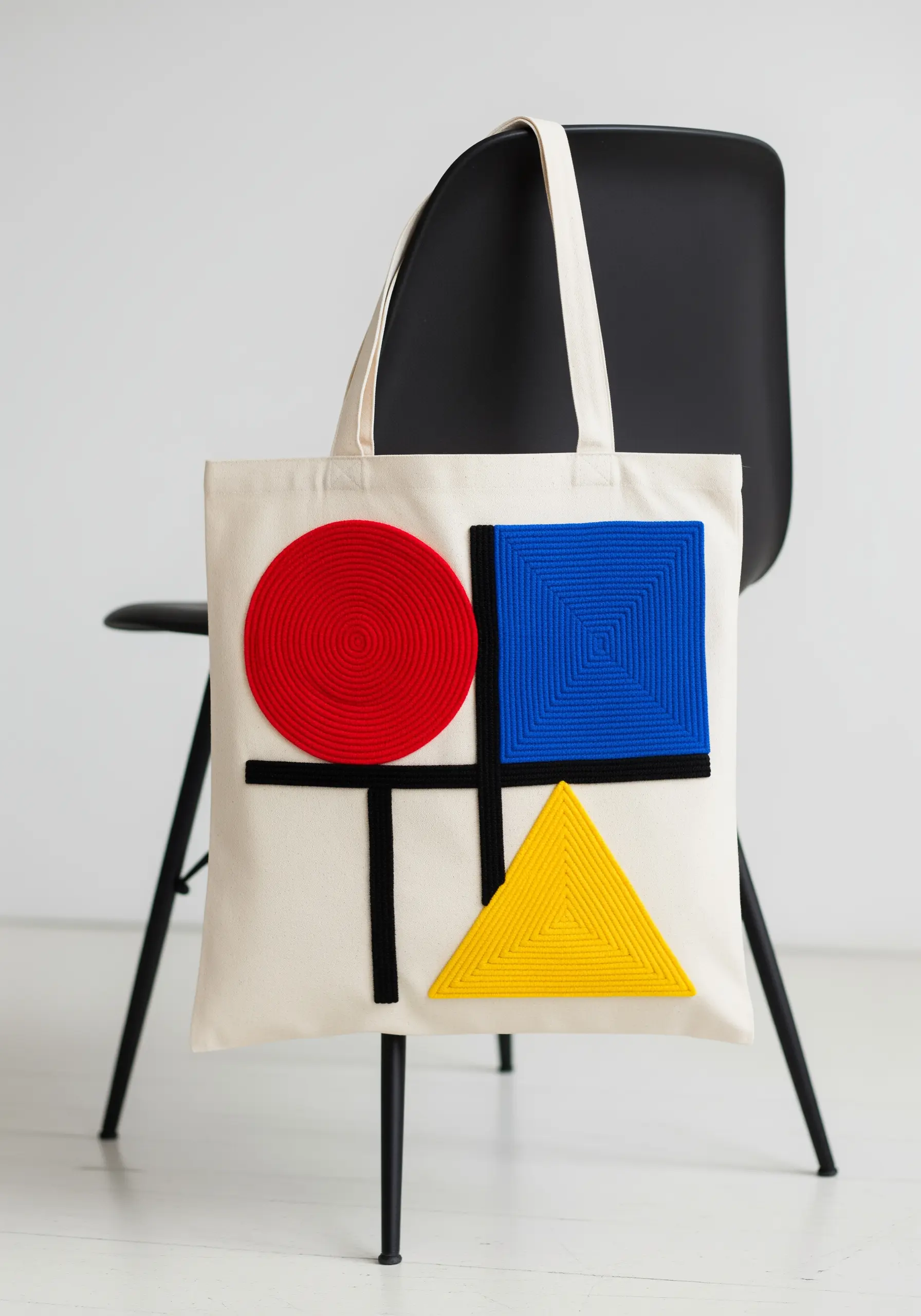 Mondrian-inspired geometric design using couched red, blue, and yellow yarn on a tote bag.