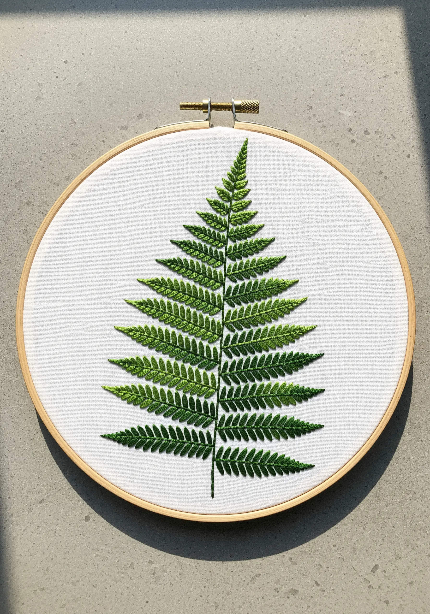 A precisely embroidered green fern leaf on a clean white fabric background.