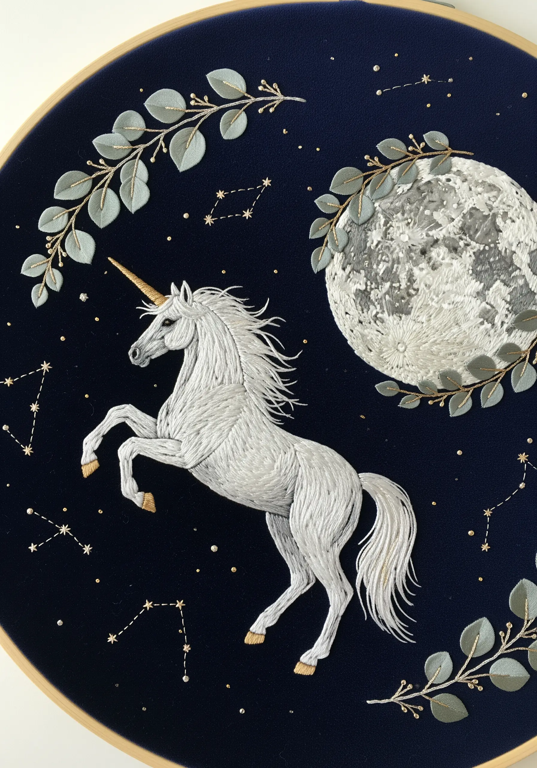 Thread-painted white unicorn on dark blue fabric with a textured moon and gold stars.