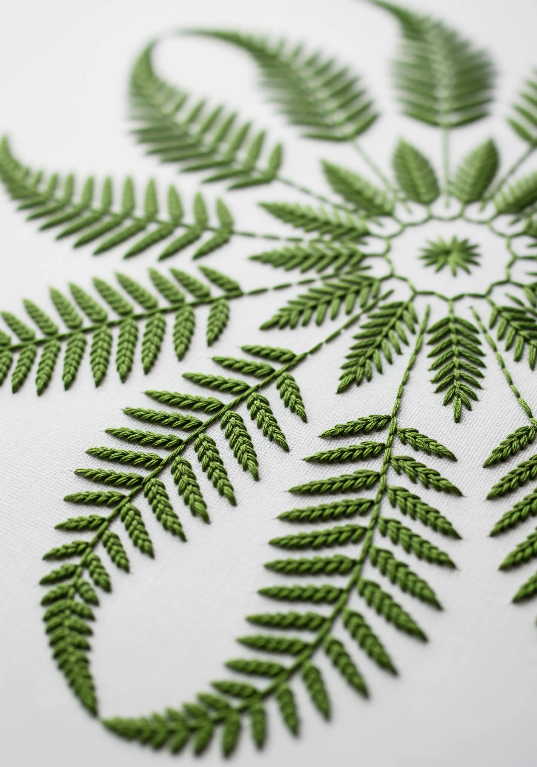 A close-up of a highly detailed green fern mandala on white fabric.